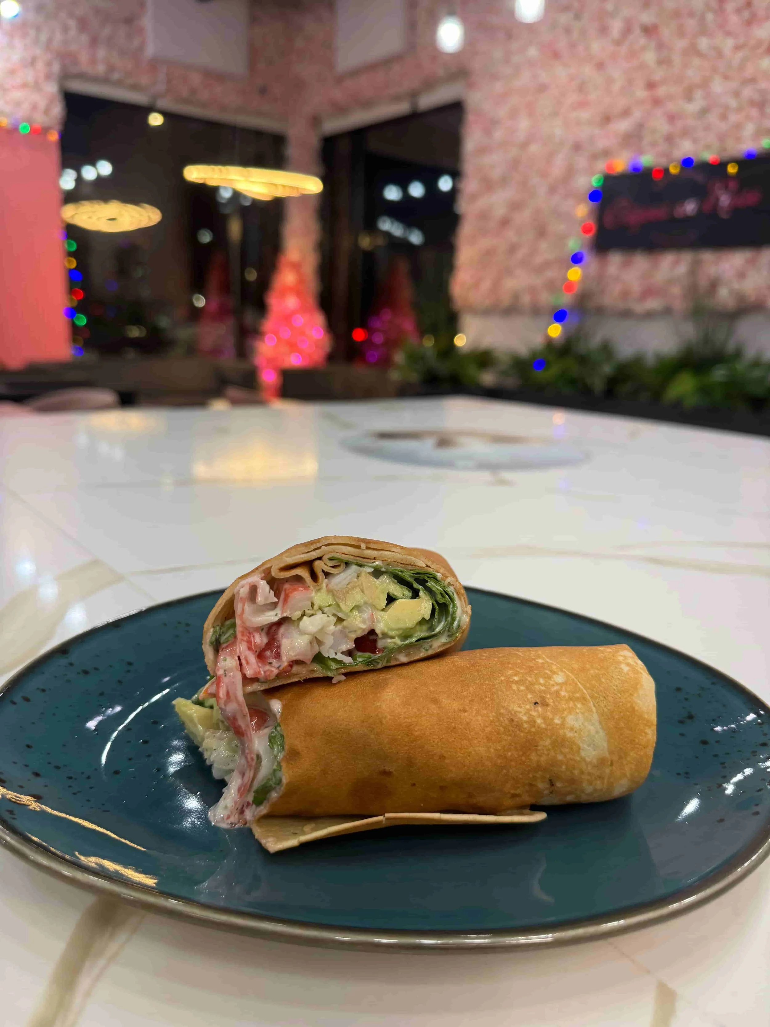 A partially eaten wrap on a blue plate with a snowy restaurant interior and holiday decorations in the background.