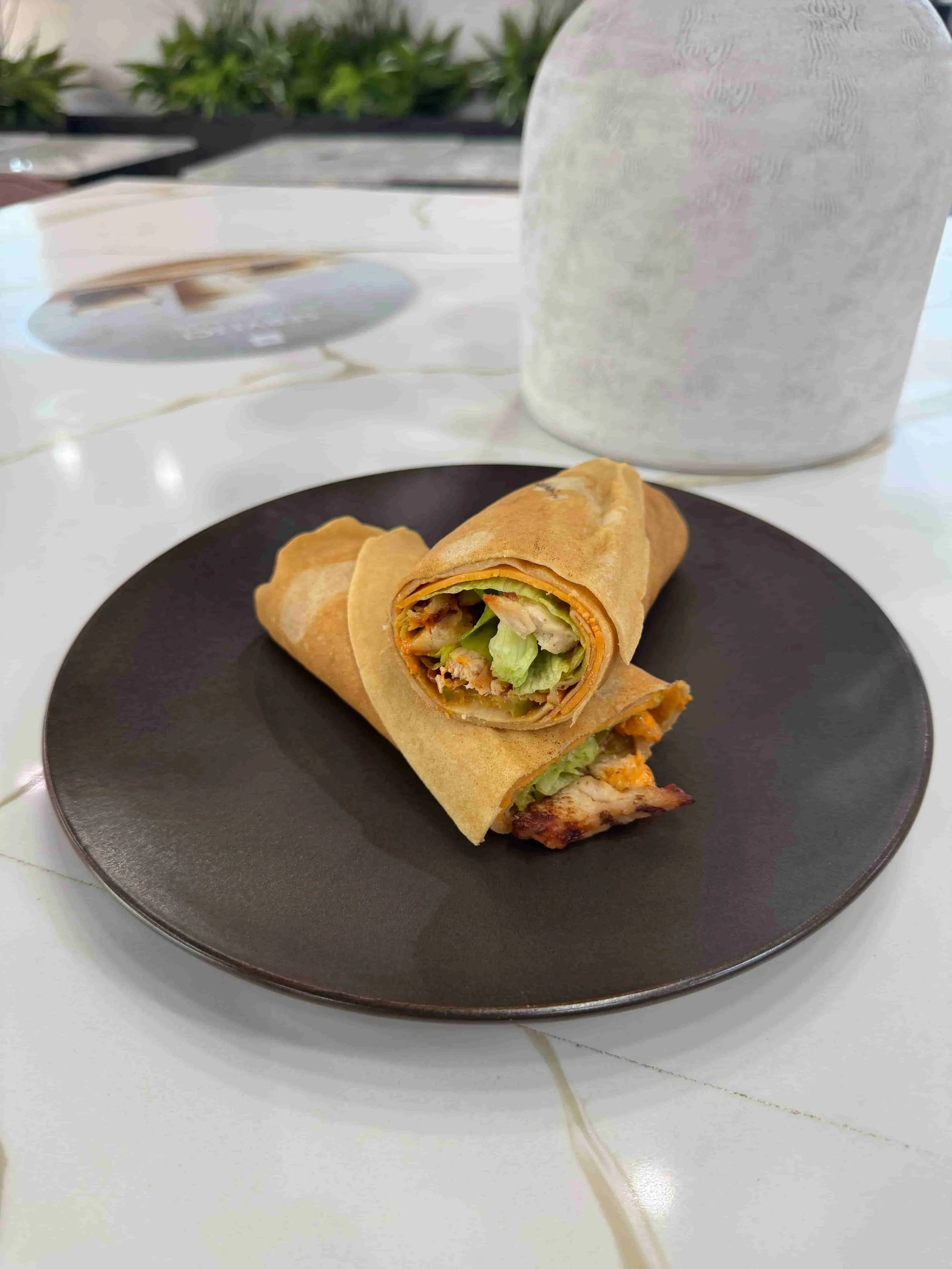 Two spring rolls with visible shredded lettuce, carrots, and chicken filling on a black plate, with a white mug in the background on a white table.