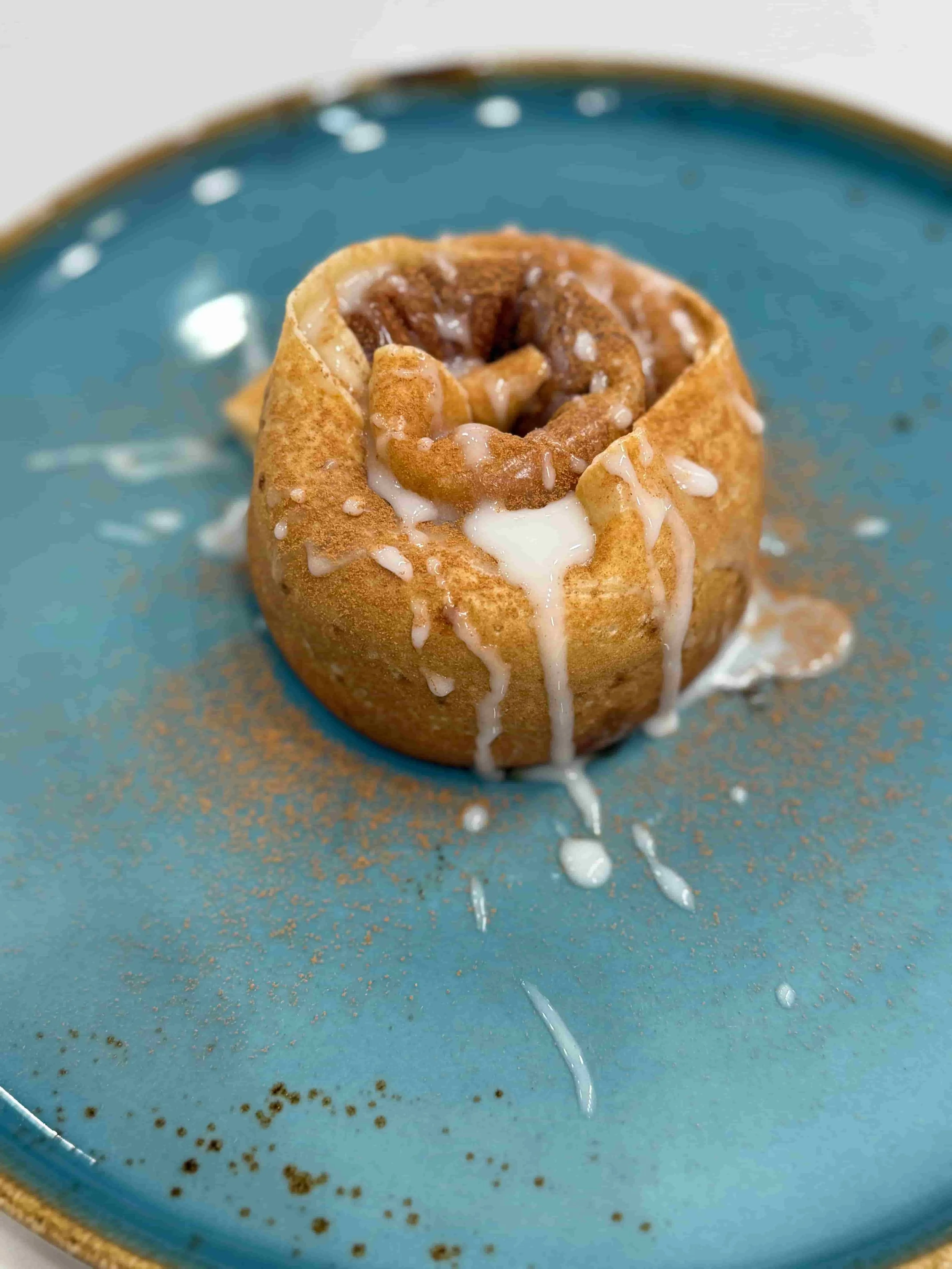 A cinnamon roll topped with white icing on a blue plate.