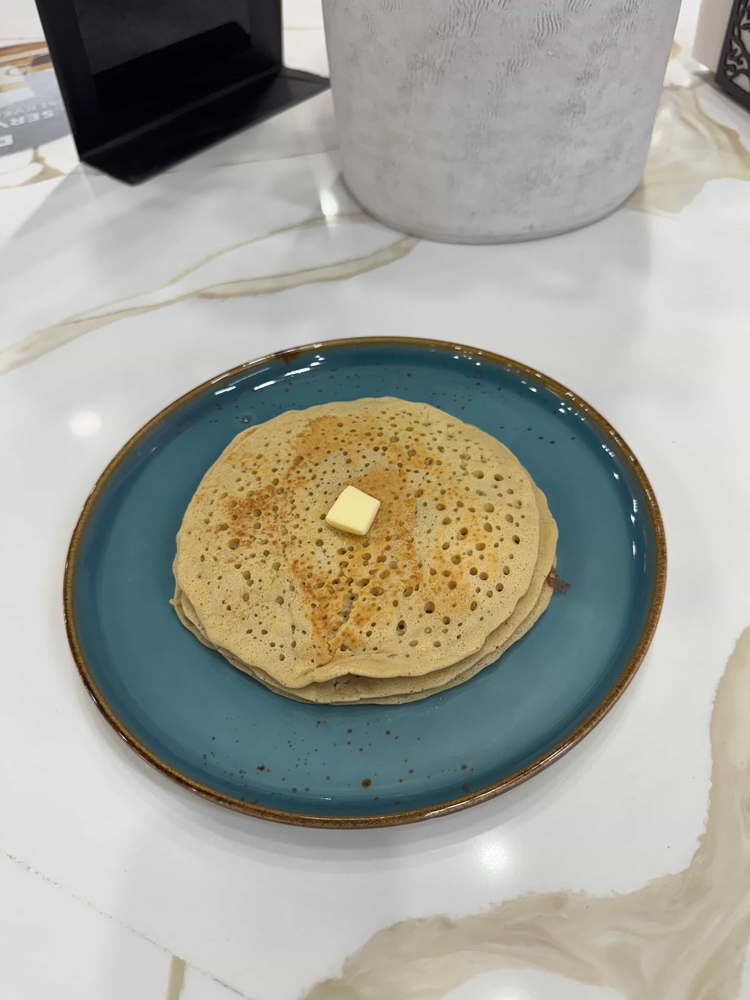 Stack of three crepes with a pat of butter on top, served on a blue plate.