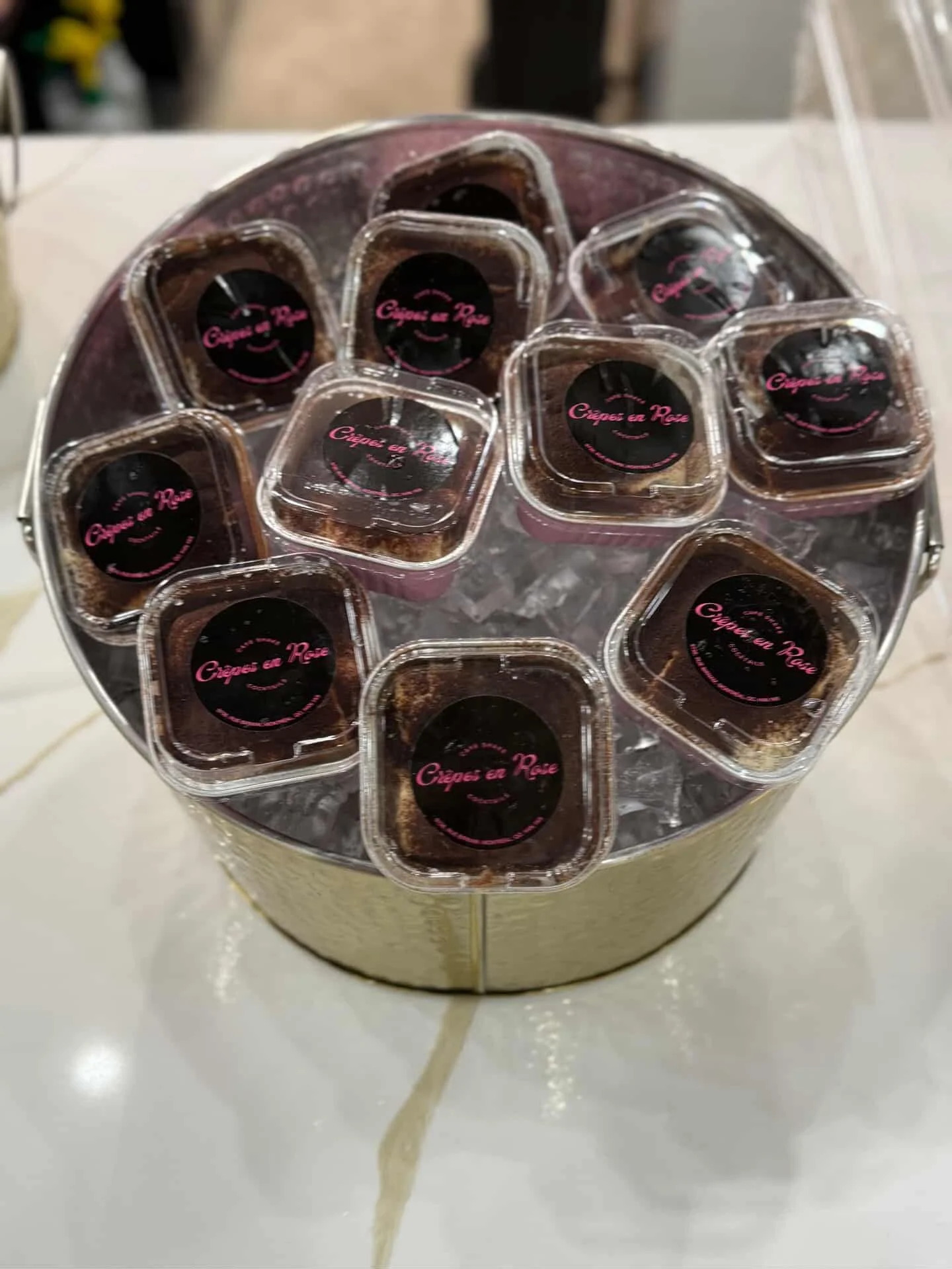 A circular display of small square containers labeled "Crêpes en Rose," arranged on a bed of ice.