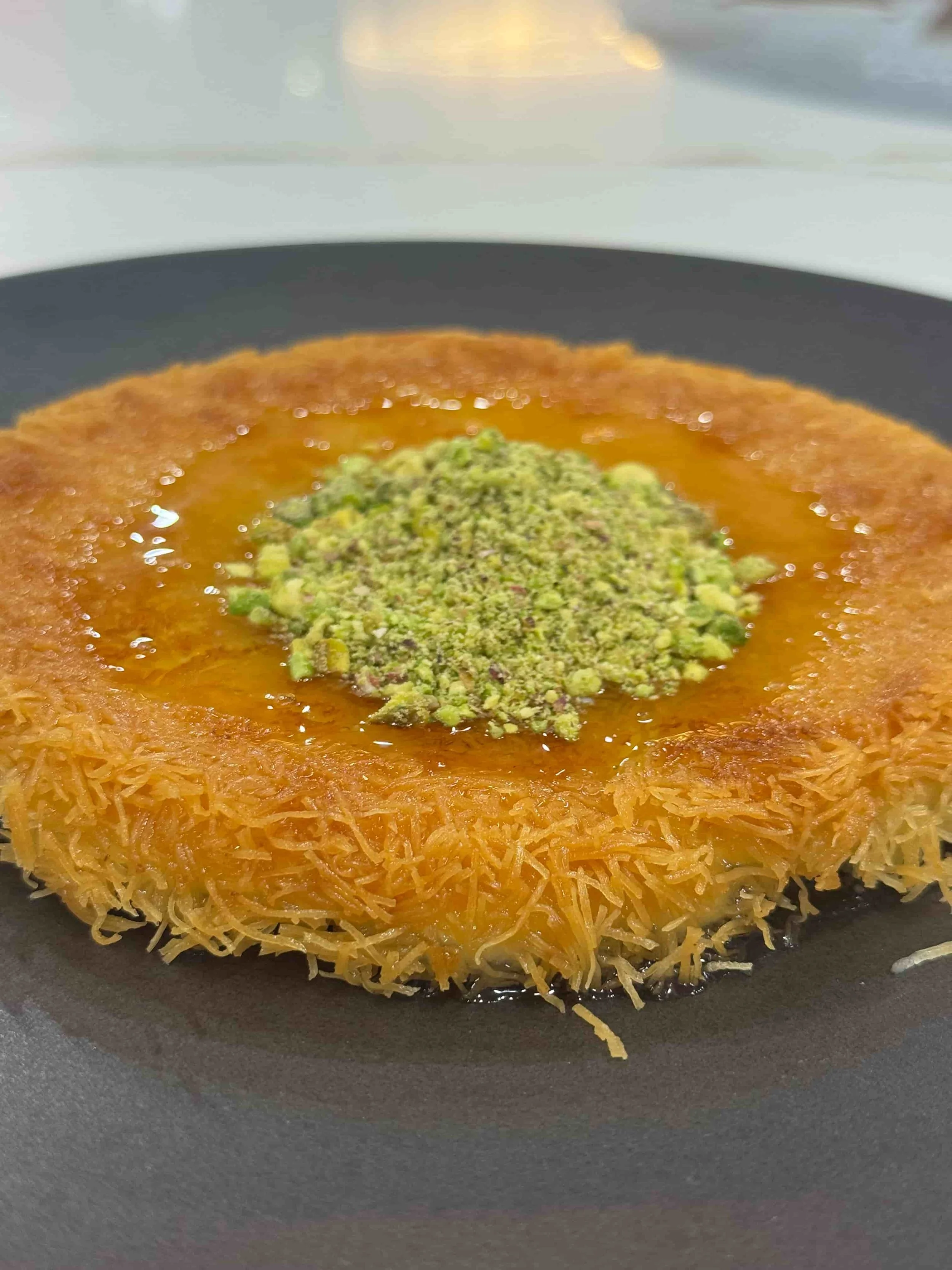 Layered dessert with a shredded phyllo crust, topped with syrup and chopped pistachios.