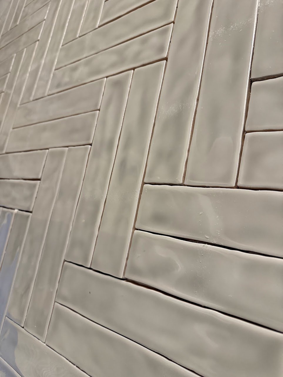Close-up view of beige ceramic tiles arranged in a herringbone pattern with narrow grout lines.