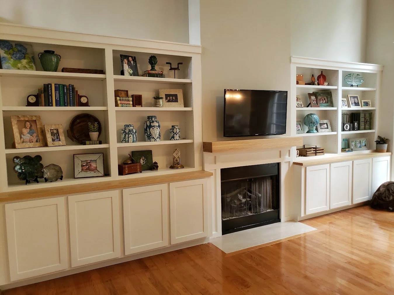 Living room with built-in white bookshelves, a fireplace, a mounted flat-screen TV, and hardwood floors