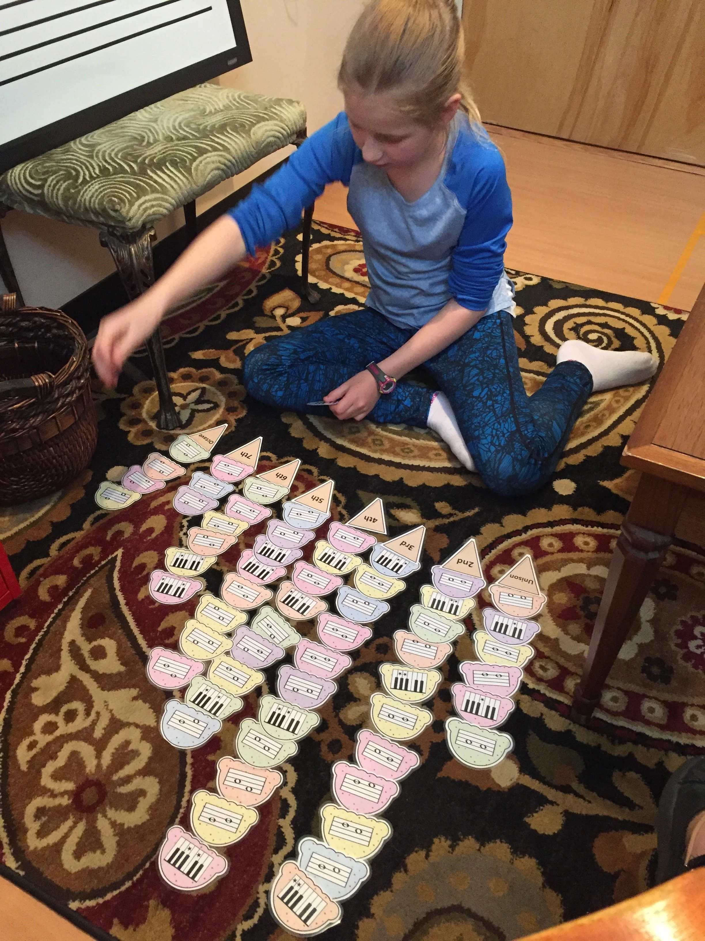 A girl sitting on a patterned rug, playing with colorful ice cream scoop-shaped paper cutouts of music notes.