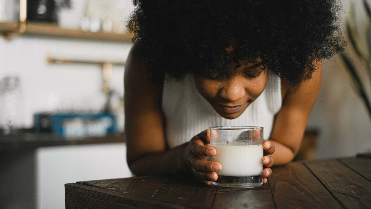 A person wearing a hooded winter jacket walking through a snowy landscape with forested hills in the background during sunset.