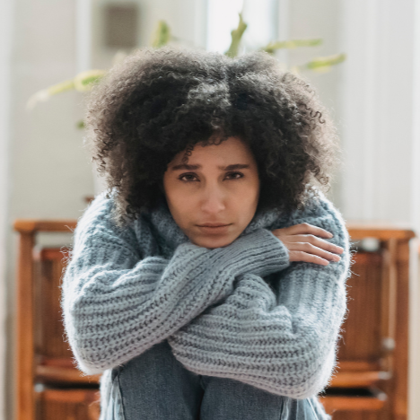 A person standing on a subway platform as a train speeds past, creating a motion blur. The person is wearing dark clothing and brown shoes.