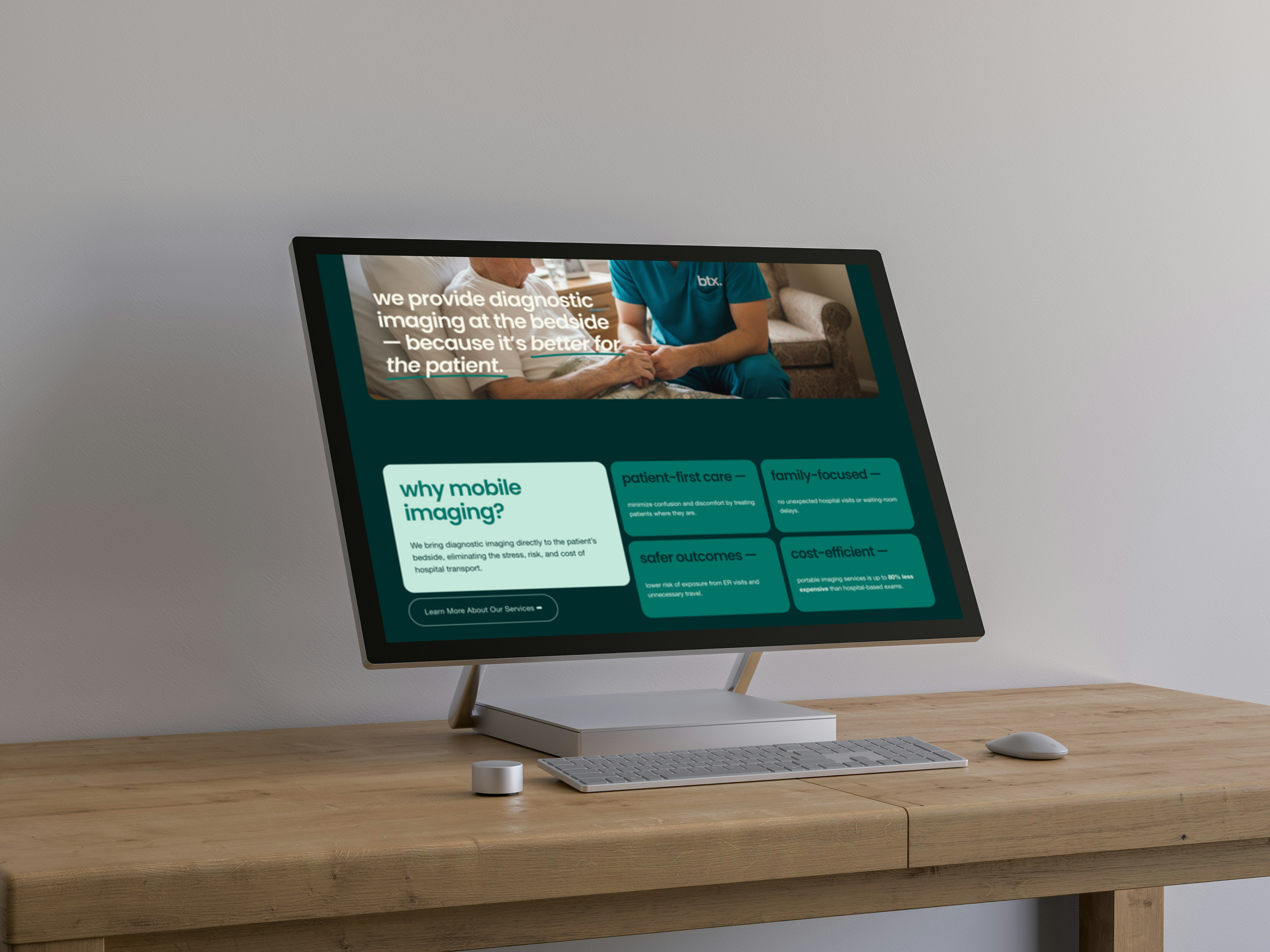 Computer monitor displaying a website about diagnostic imaging, placed on a wooden desk with a wireless keyboard and mouse inside a minimalist room.