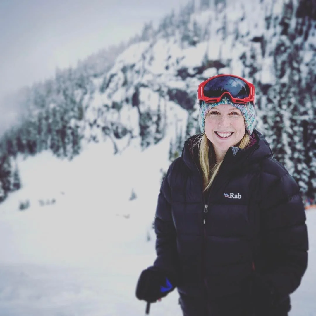 Person in ski gear smiling on a snowy mountain backdrop.
