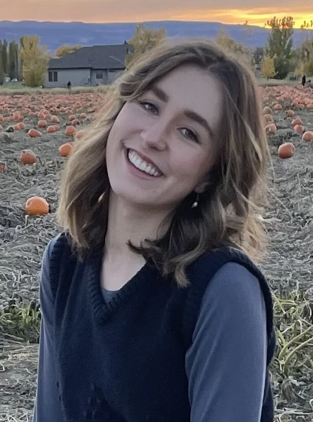 A young woman with light brown hair and a bright smile posing in a pumpkin patch at sunset.
