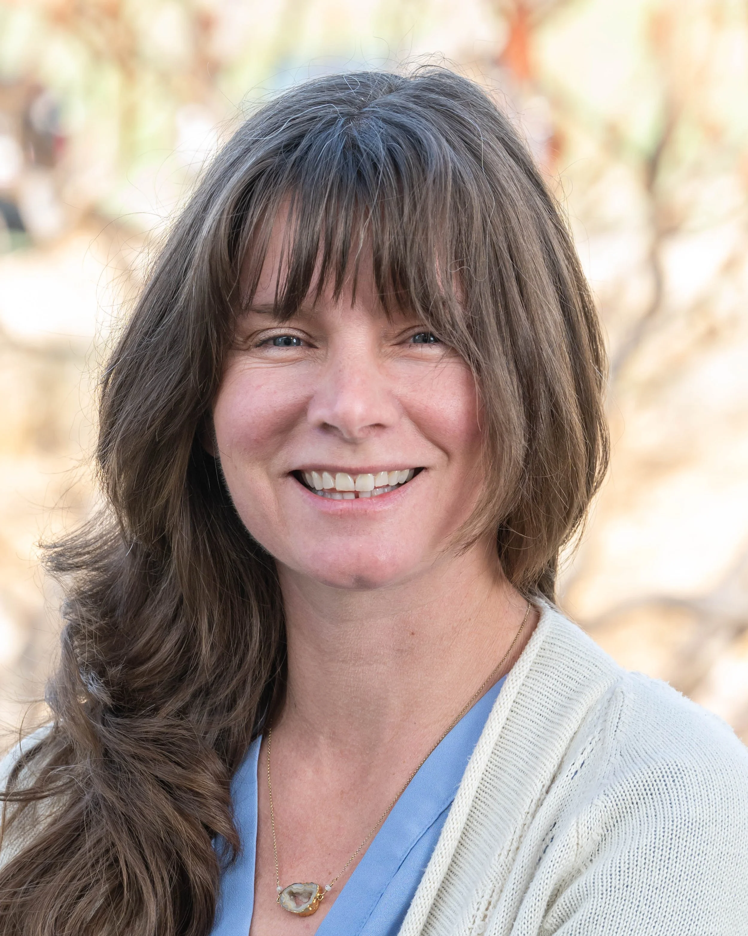 Close-up of a woman with short, brown hair smiling outdoors.