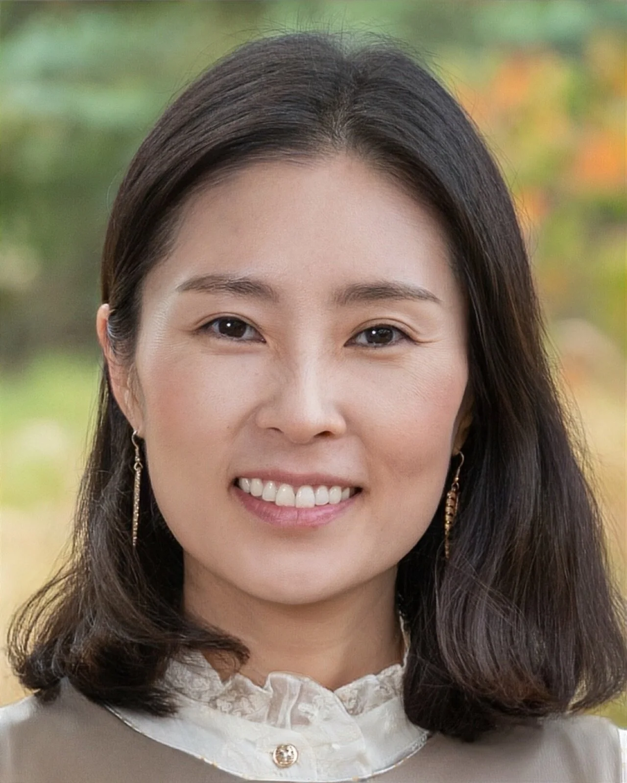 A young woman with shoulder-length dark hair smiling, wearing a pale pink striped button-up shirt, against a brown and beige abstract background.