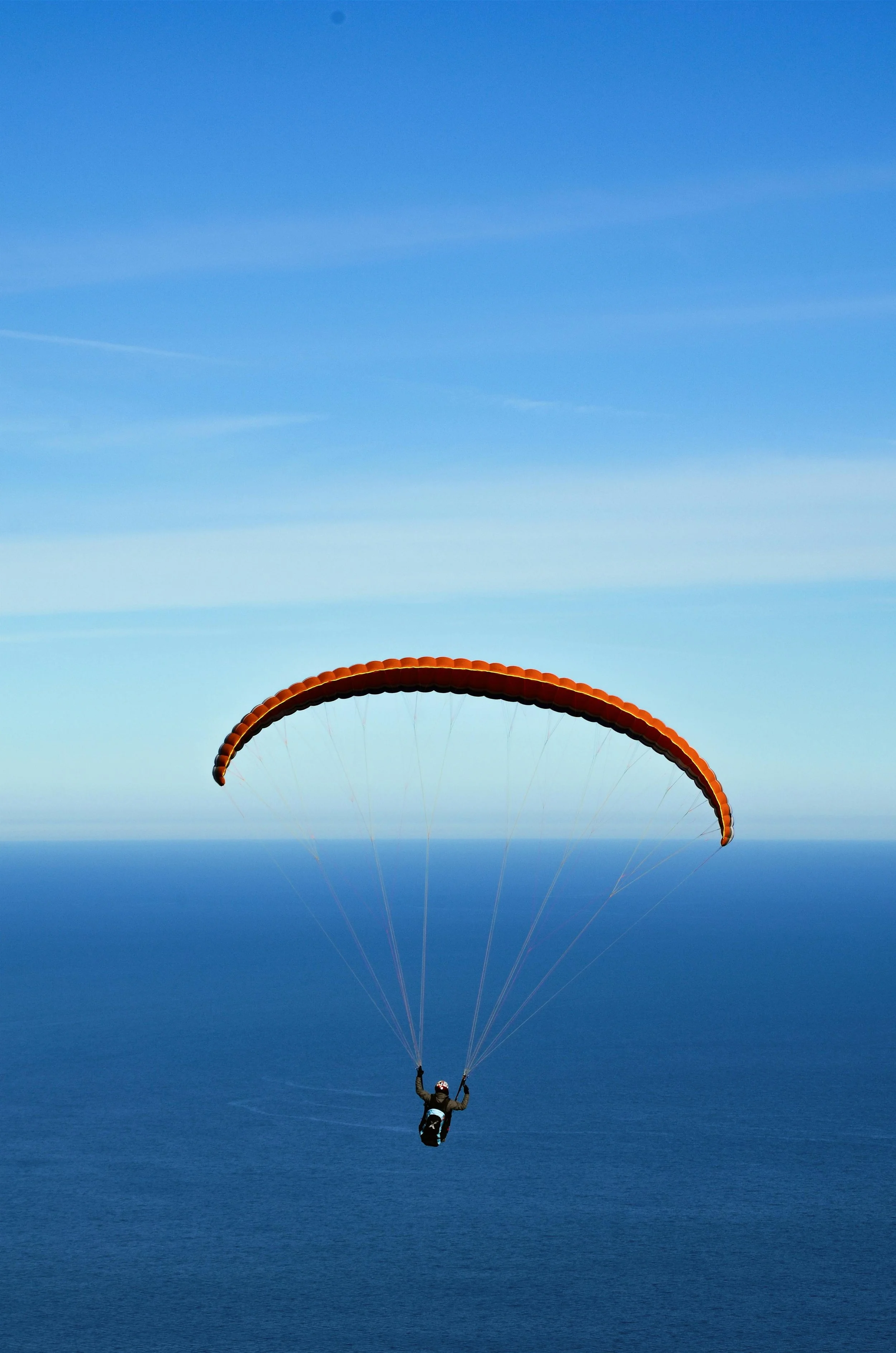 A skydiver descending with a parachute over a body of water, with a clear blue sky in the background.