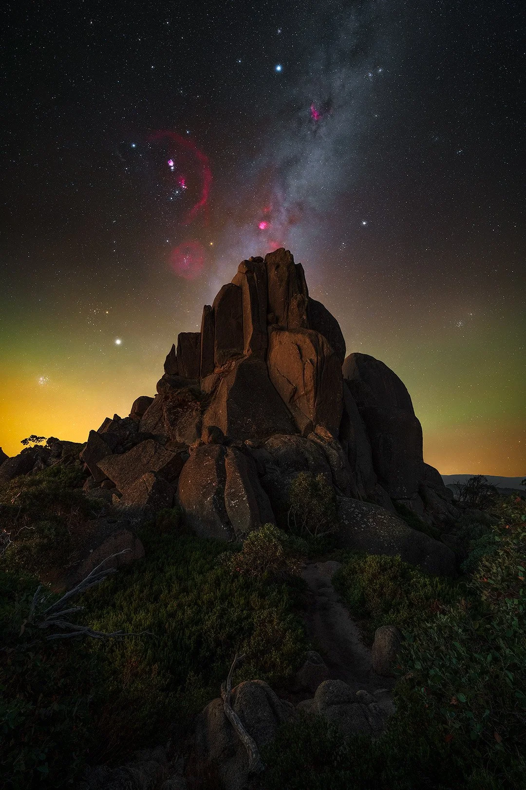A rocky formation under a starry night sky with the galaxy and nebulae visible.