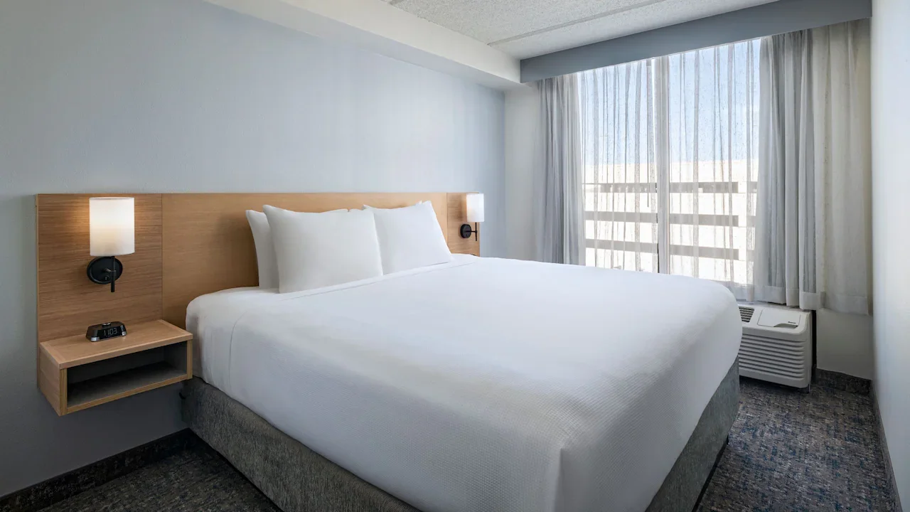 Clean hotel room with a large bed, two bedside lamps, a digital clock, and a window with curtains.