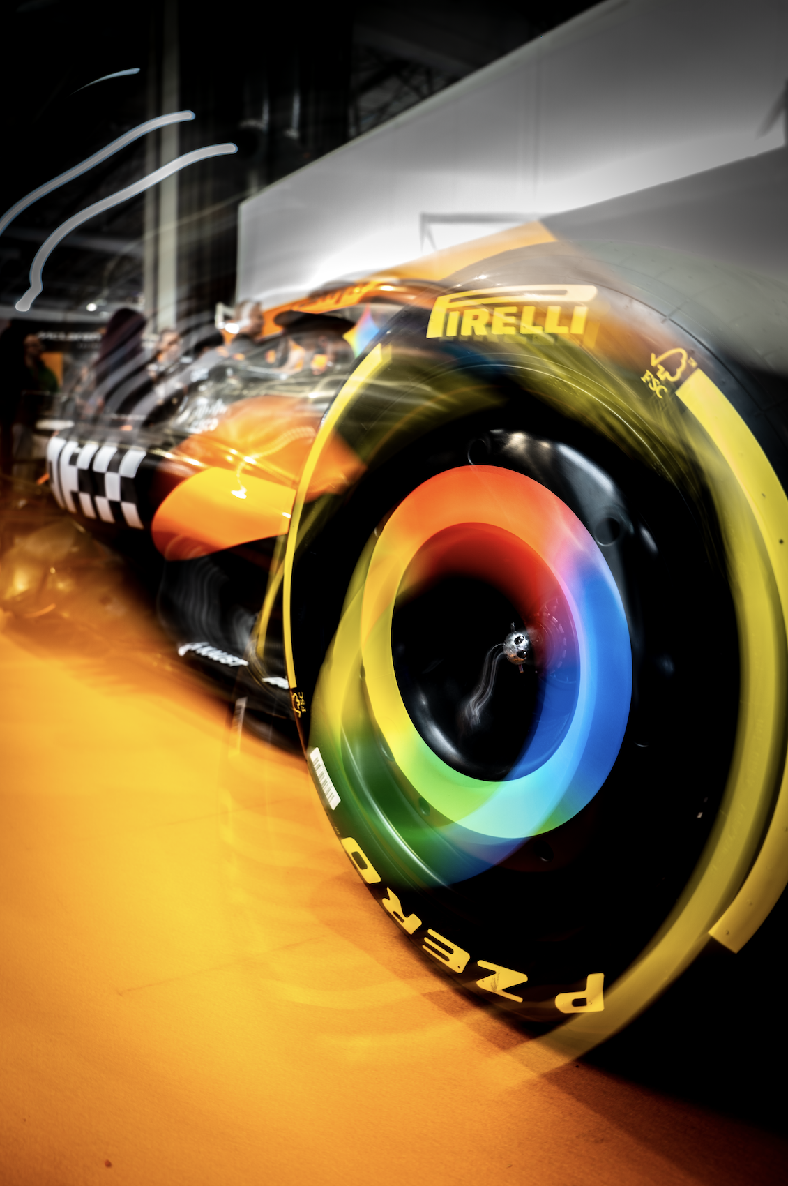 Close-up of a racing car wheel with rainbow-colored tire and Pirelli branding, blurred background indicating motion.