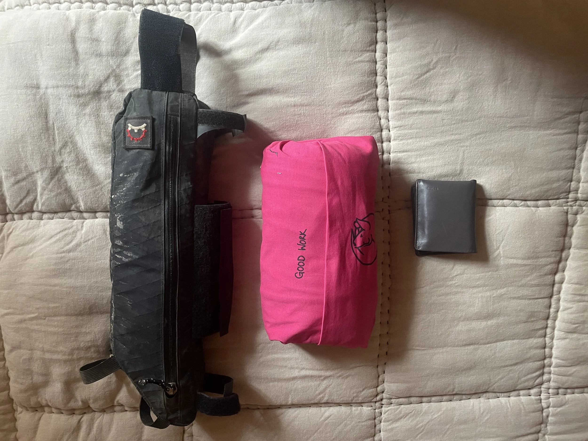 A frame bag, a Fold and Roll and a wallet on a quilt