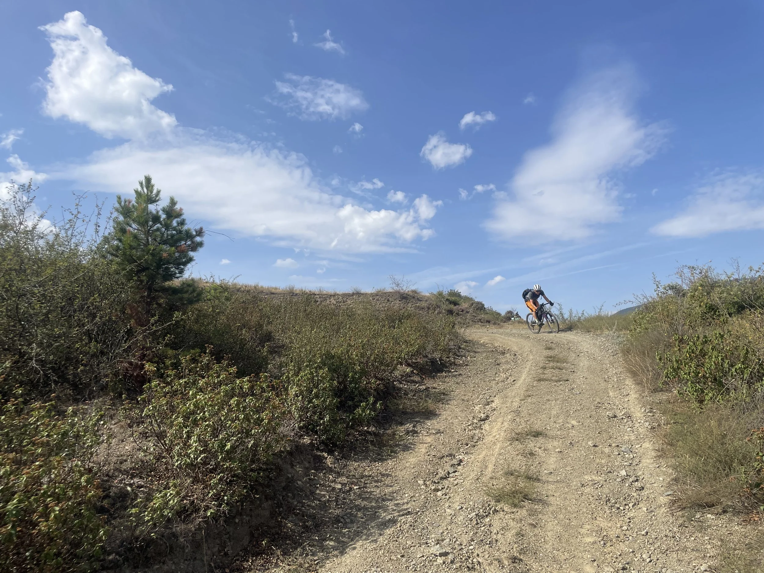 A cyclist on a gravel track with blue sky and scrubland