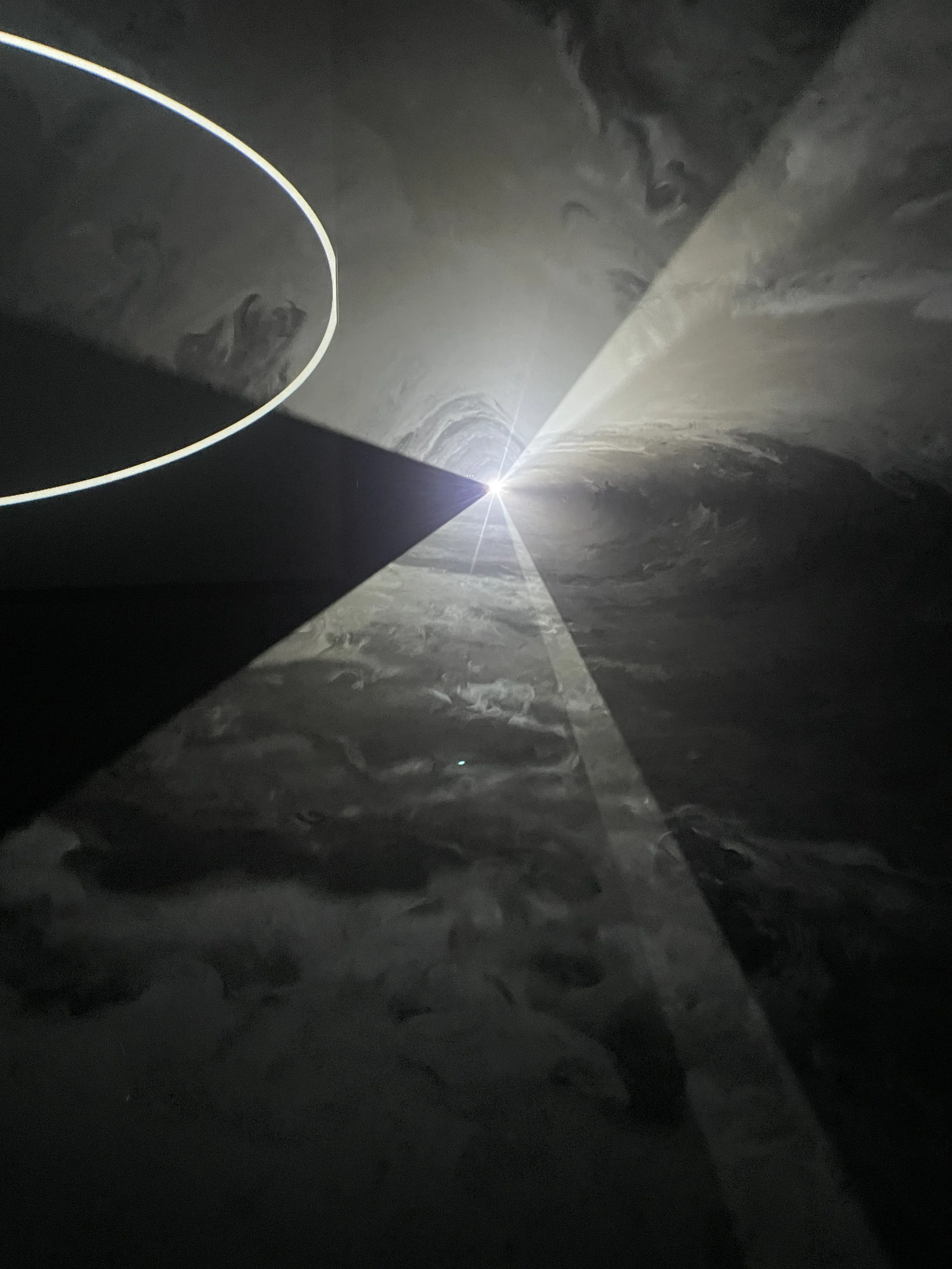 A geometric pattern of grey and white - some segments are textured with smoke whorls - radiating from a bright spot of light.