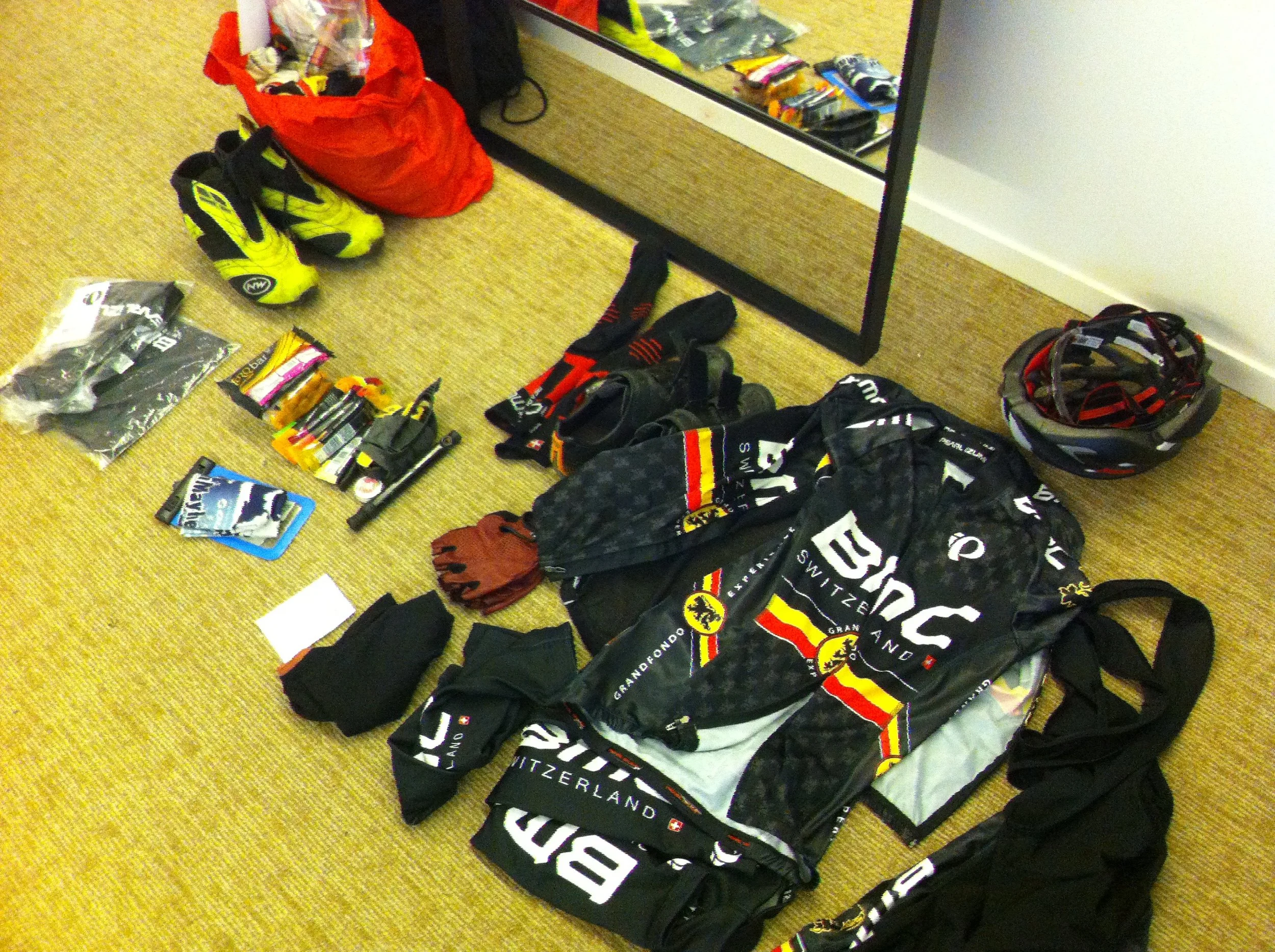 A full cycle kit, shoes and helmet, gels and papers laid out on a hotel room floor