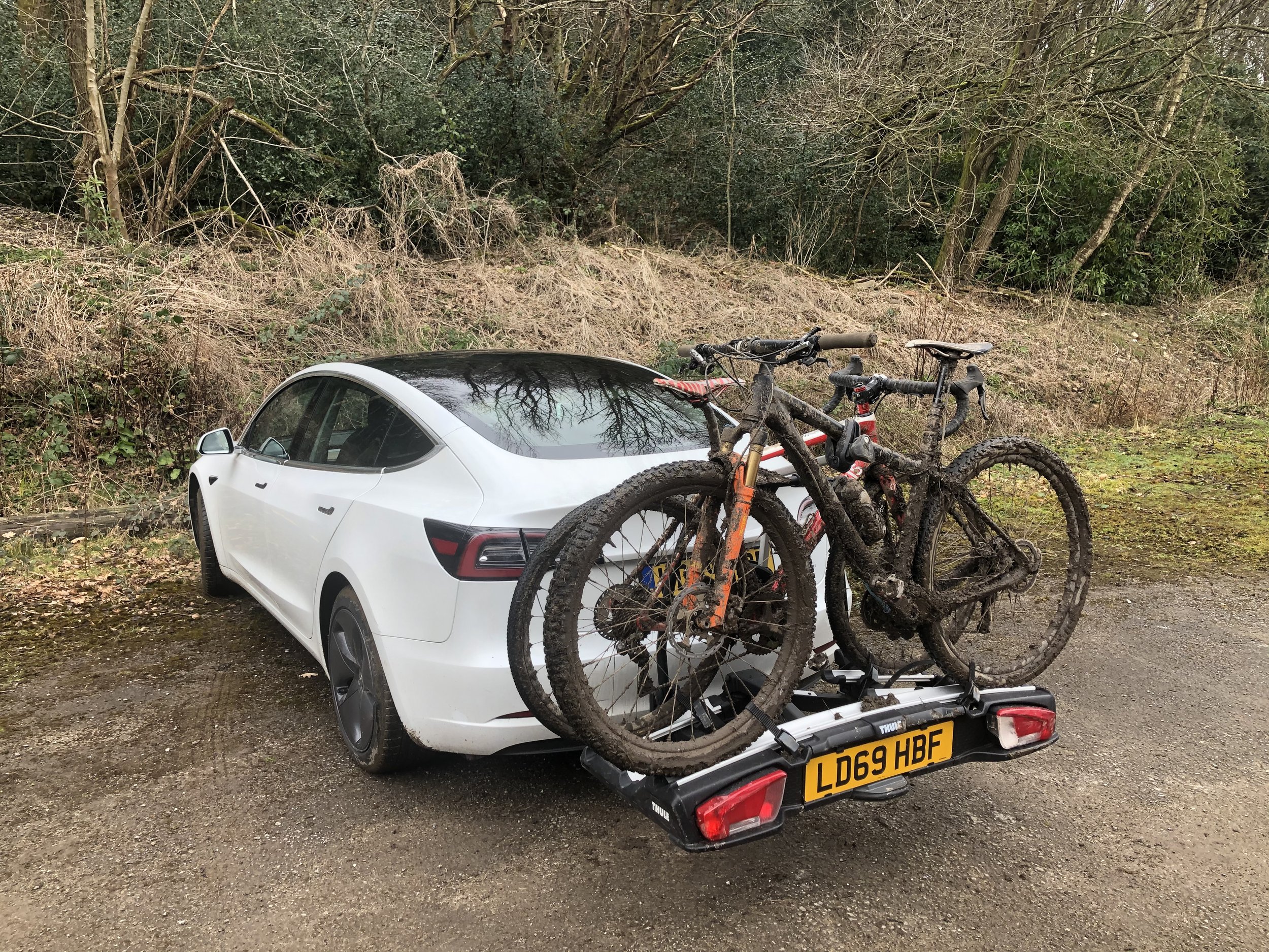 A white Tesla with a bike rack carrying two muddy mountain bikes
