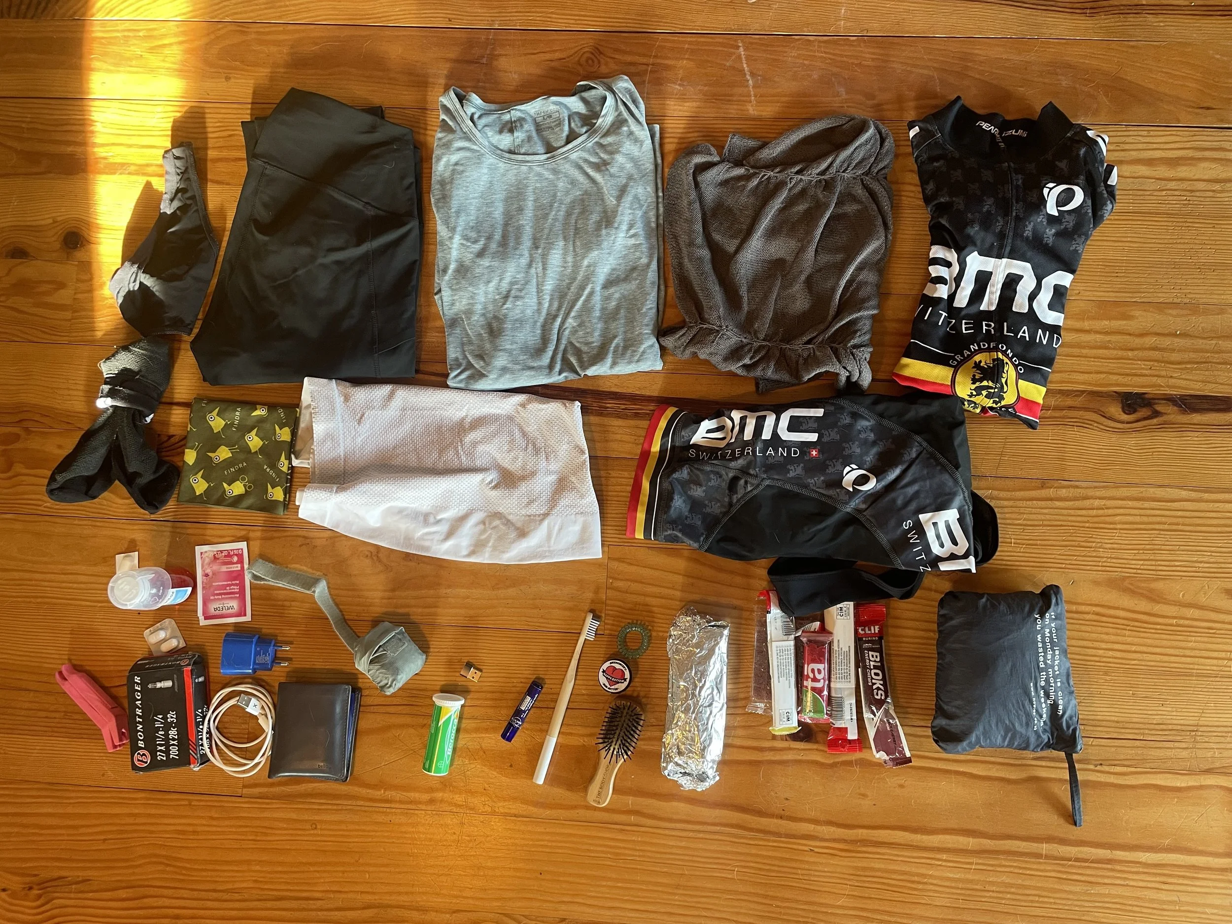 Folded cycling clothes, toiletries, wallet and cycling tools laid out on a wooden floor