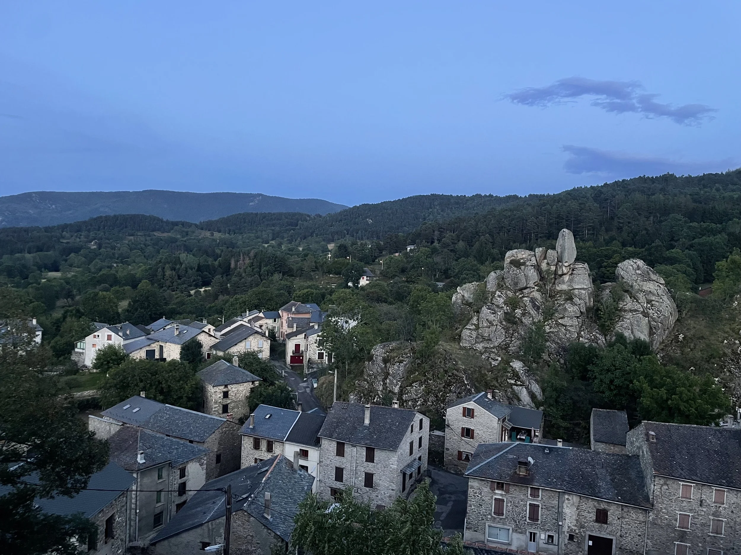 Houses clustered around a rocky outcrop with fir covered mountains behind