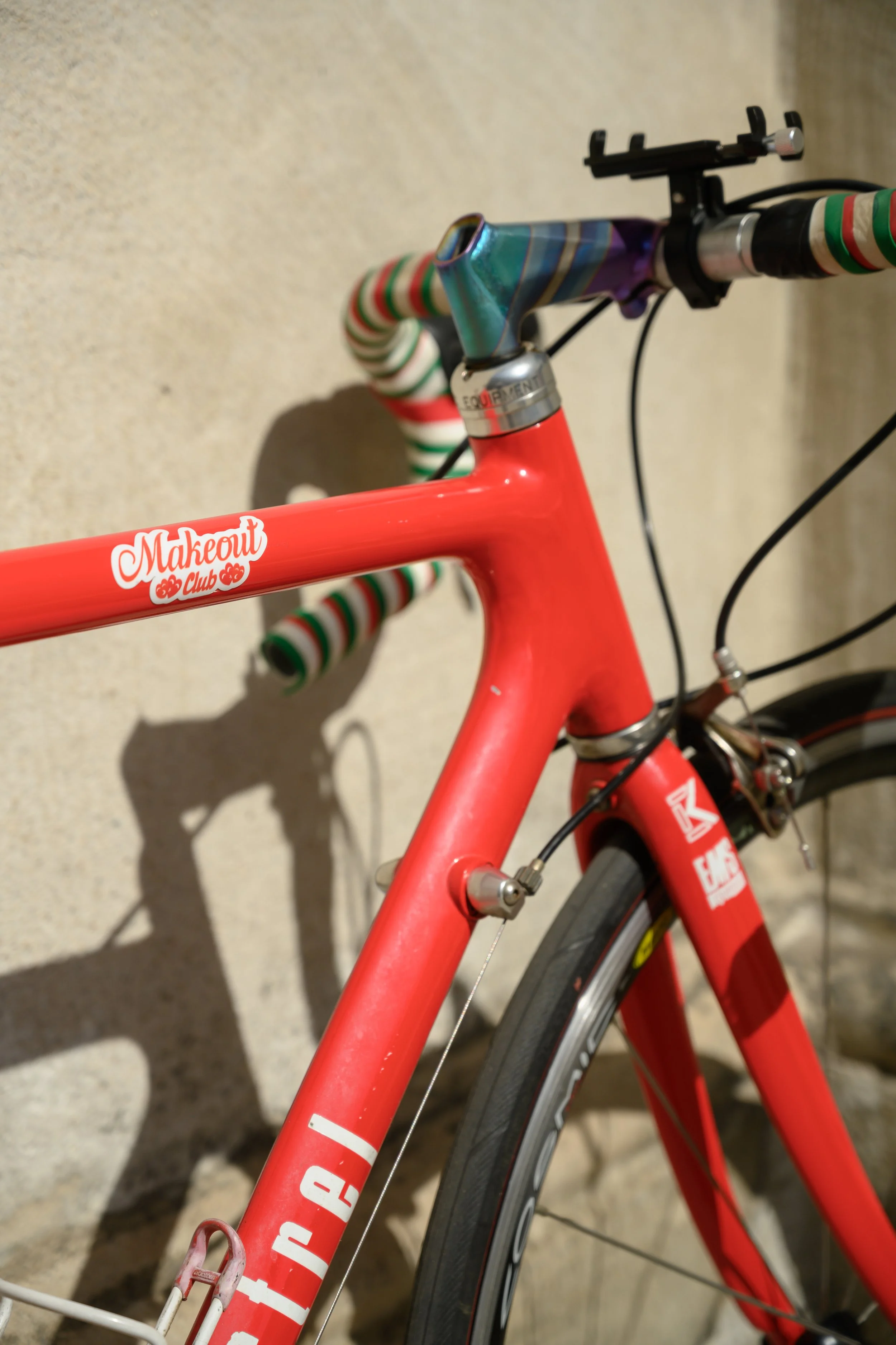 Close-up of a red bicycle with a rainbow-colored handlebar and a sticker that reads 'Makeout Club'.