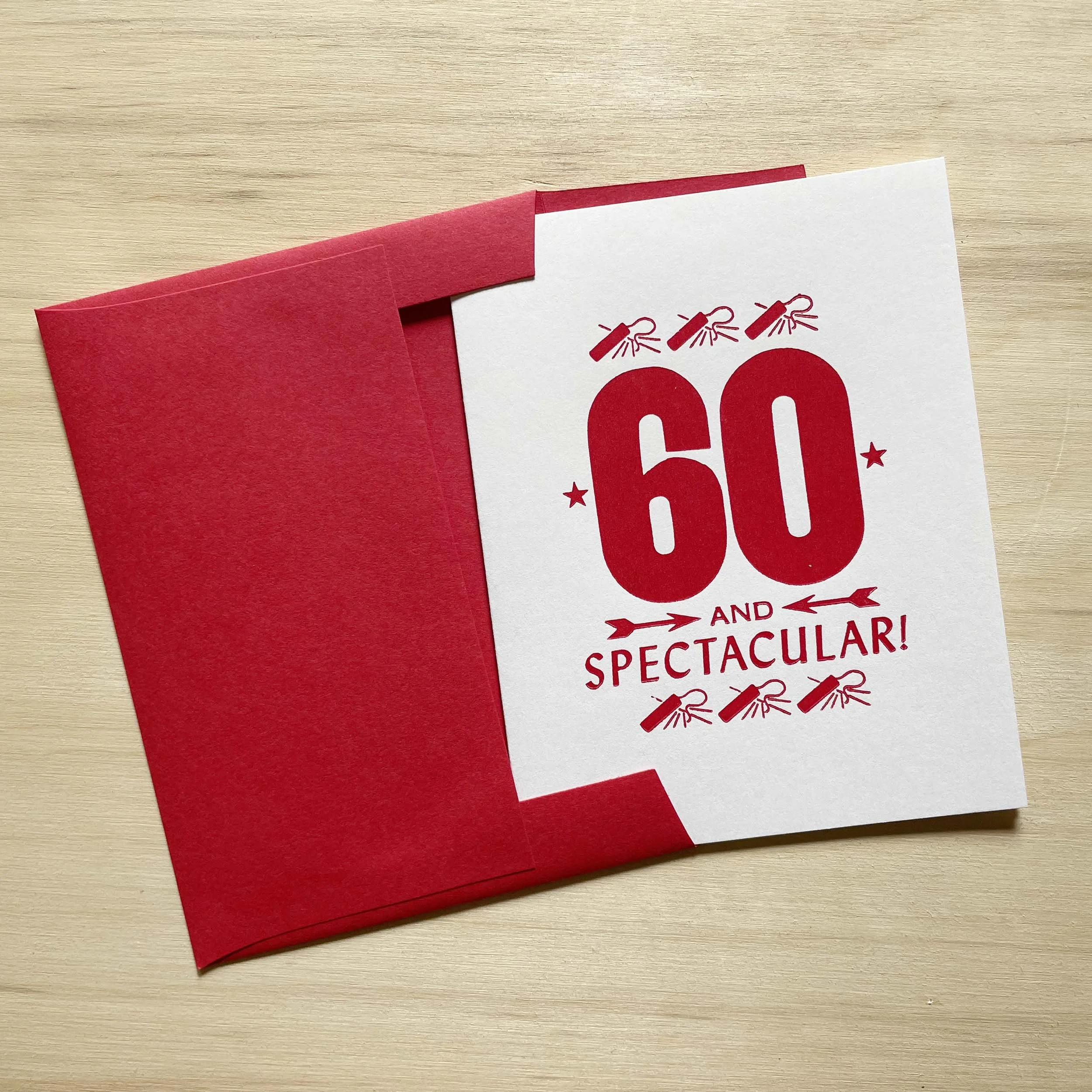 60 and Spectacular card features a bold 60 with smaller words AND SPECTACULAR. Letterpress ornaments add decoration. Vibrant red ink on white paper. Red envelope.