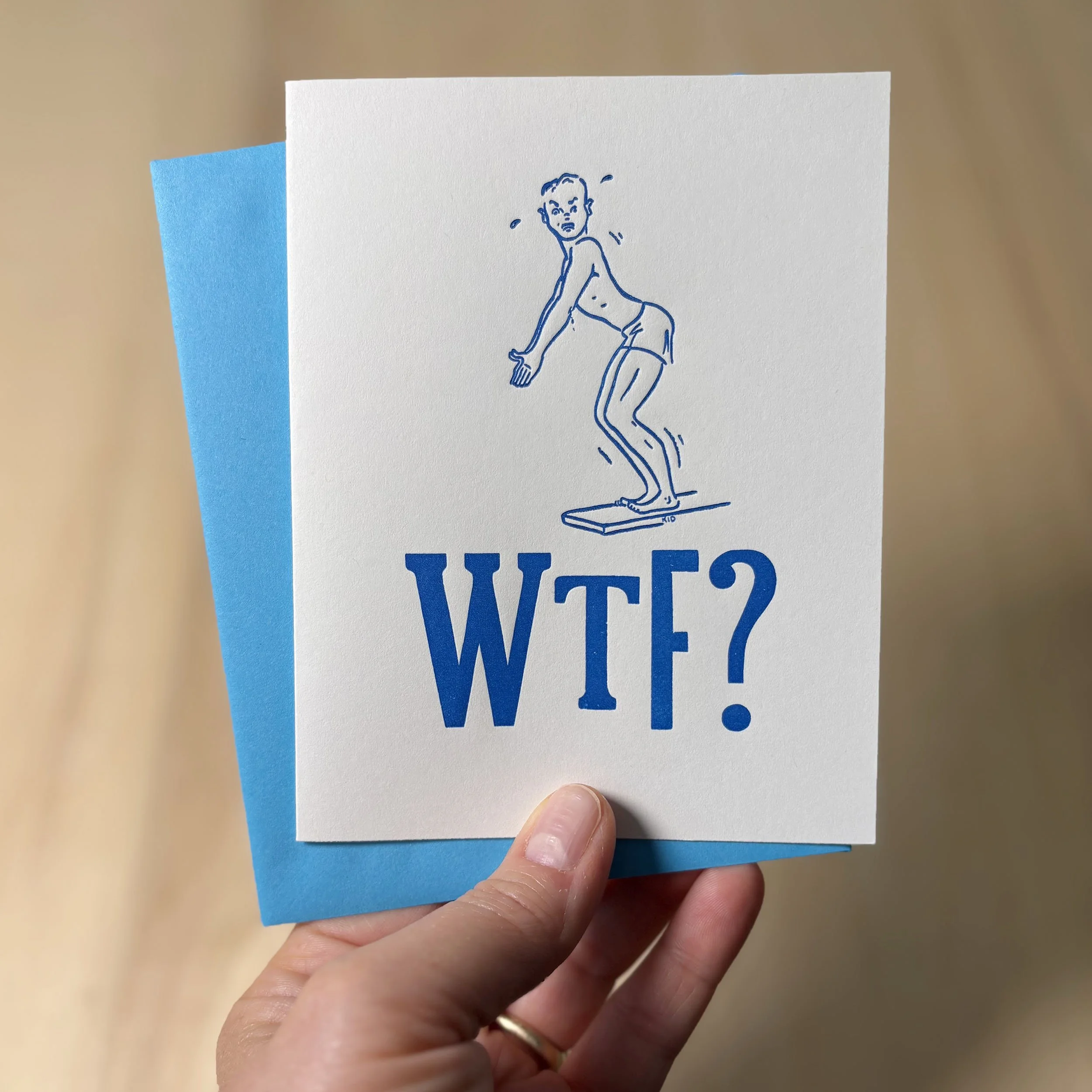 White letterpress card with a cartoonish line drawing of a young man on a diving board with a confused look on his face. Large, mis-matched bold type below says, 'WTF?' Bright blue envelope.