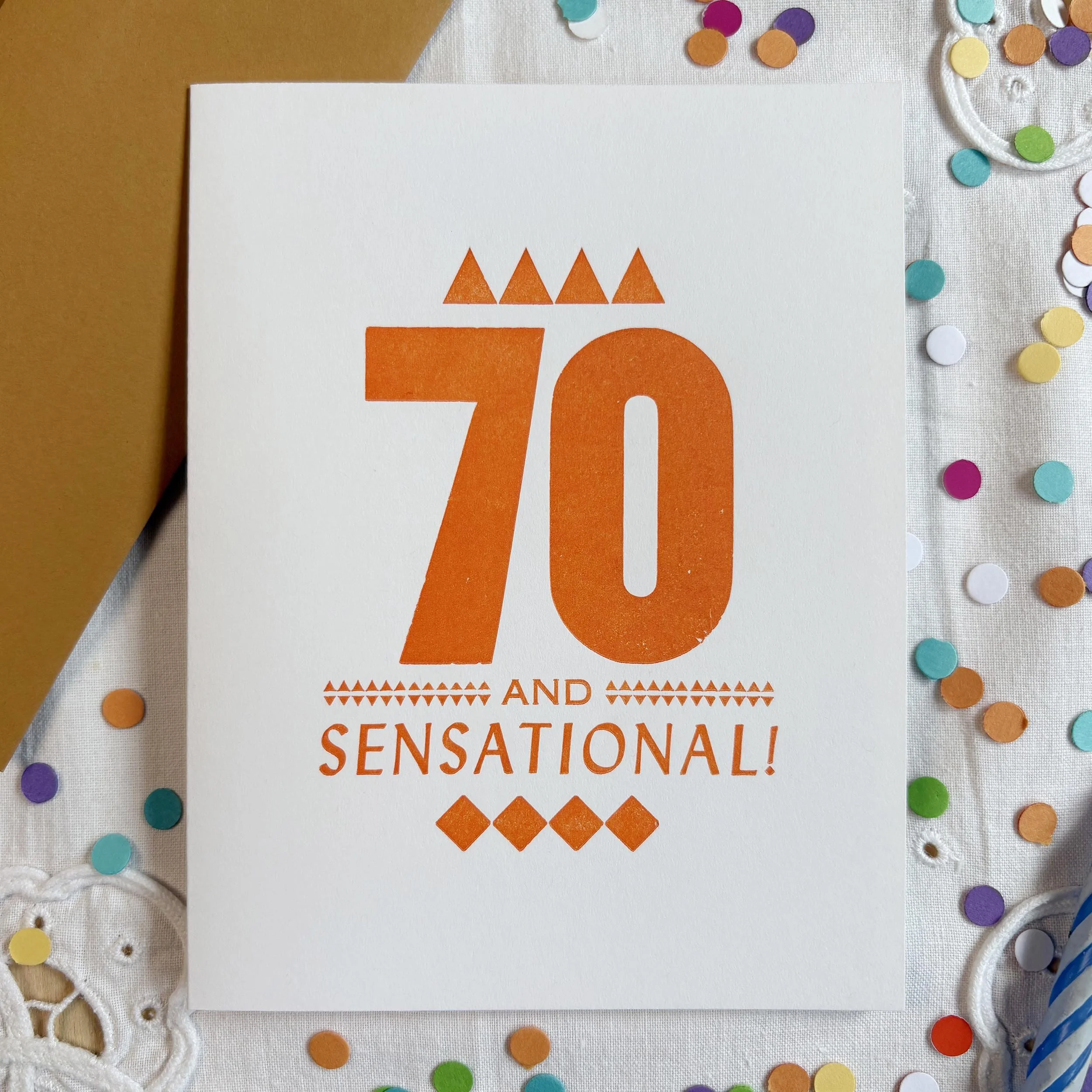 70 and Sensational card features a bold 70 with smaller words AND SENSATIONAL. Letterpress ornaments add decoration. Orange ink on white paper. Orangey brown envelope.