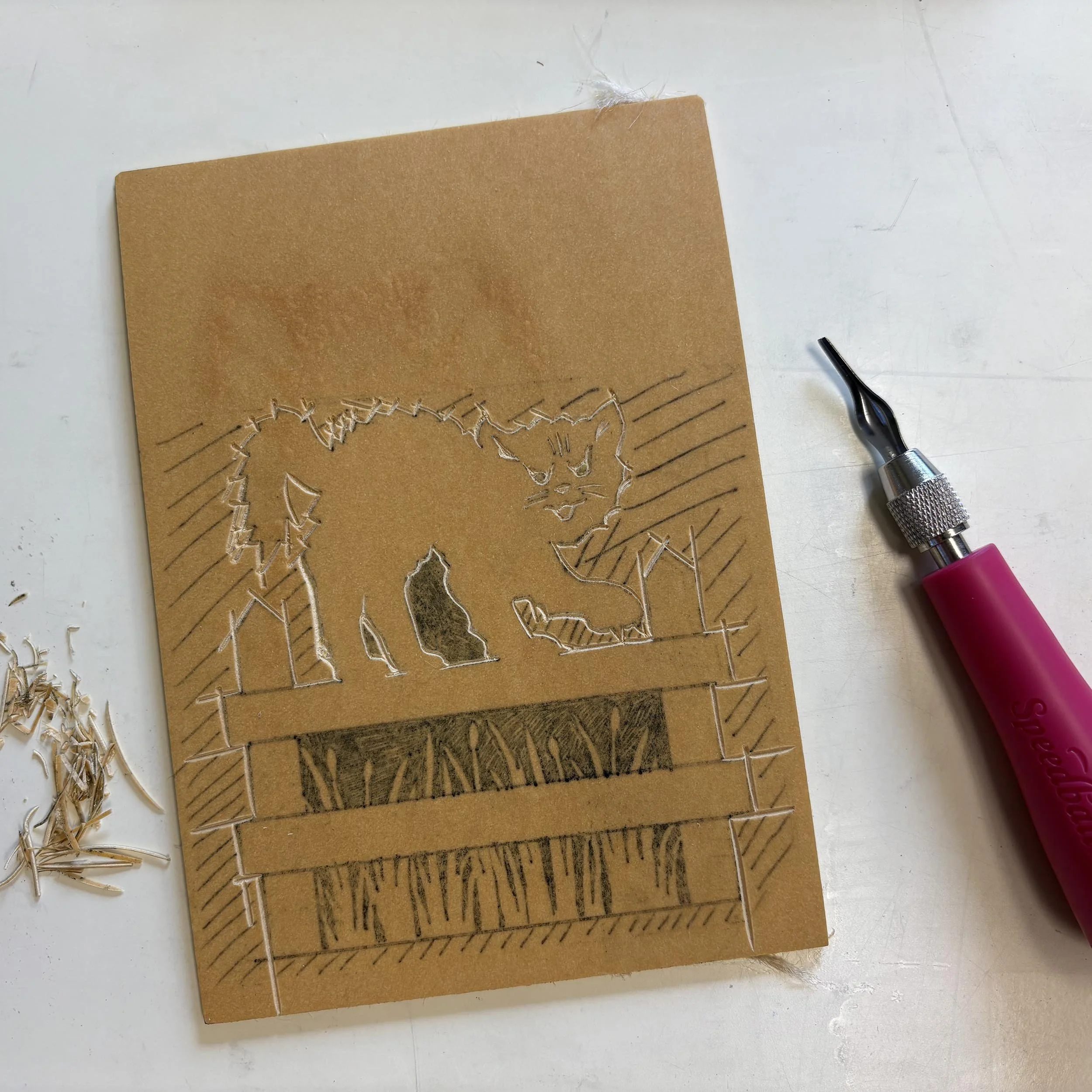A piece of tan linoleum rests on a work surface, and some has been carved away with a carving tool.