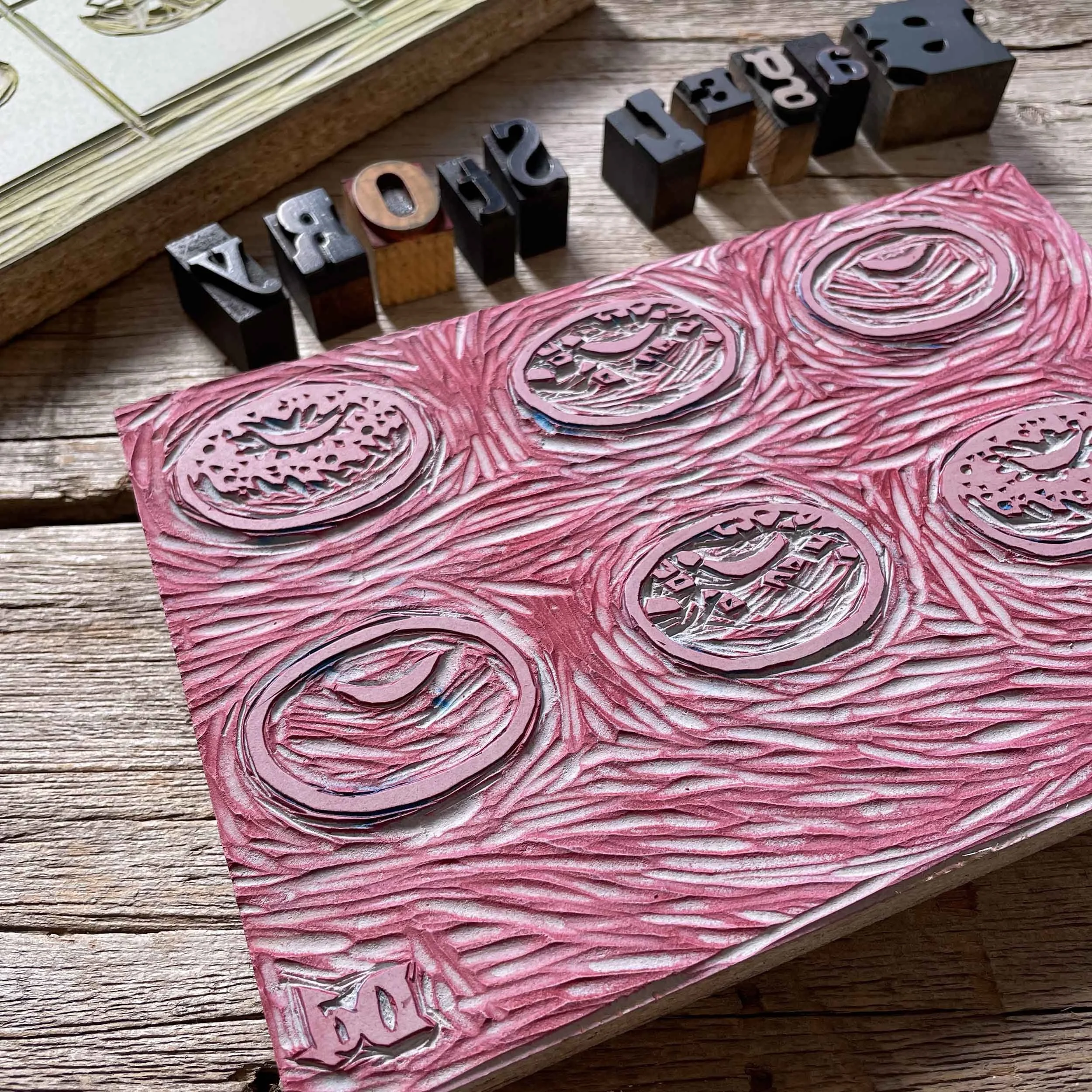 Close-up view of a red-toned linoleum printing block featuring six carved bagels. The block is rectangular and shows the texture of being carved and previously inked.