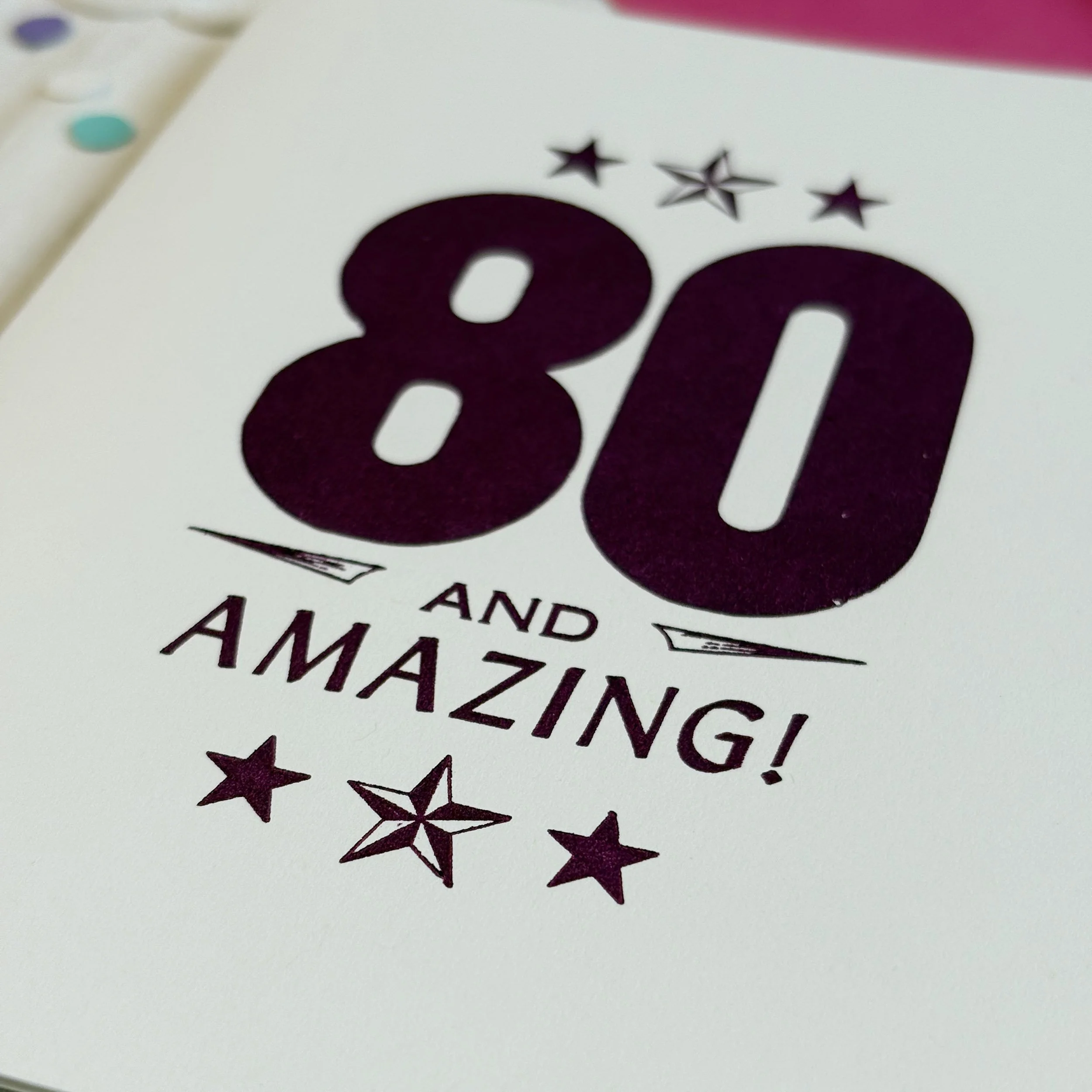 80 and Amazing card features a bold 80 with smaller words AND AMAZING. Letterpress ornaments add decoration. Dark purple ink on white paper.