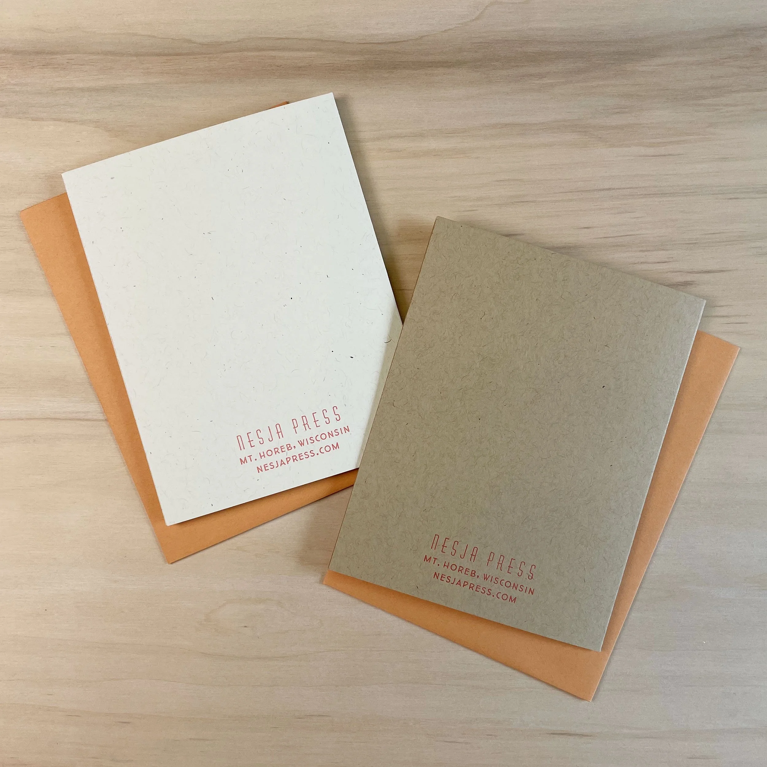 Back sides of white and kraft paper cards with Nesja Press logo and address printed small near the bottom. Orange envelopes.
