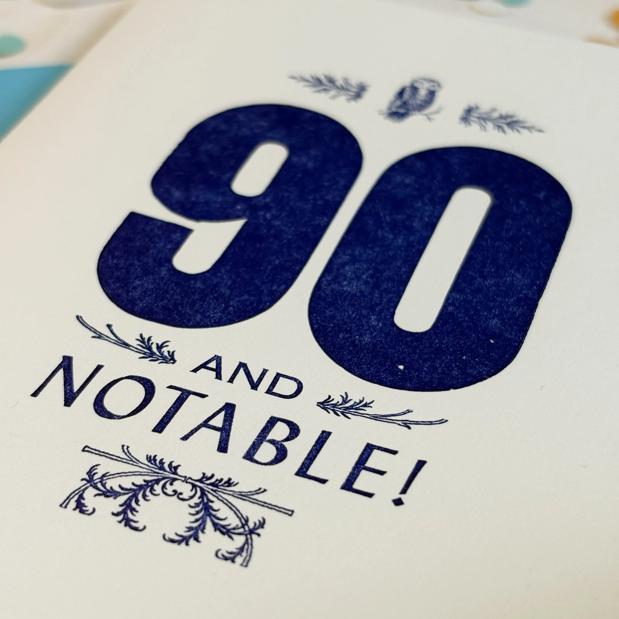 90 and Notable card features a bold 90 with smaller words AND NOTABLE. Letterpress ornaments add decoratio. Dark royal blue ink on white paper.
