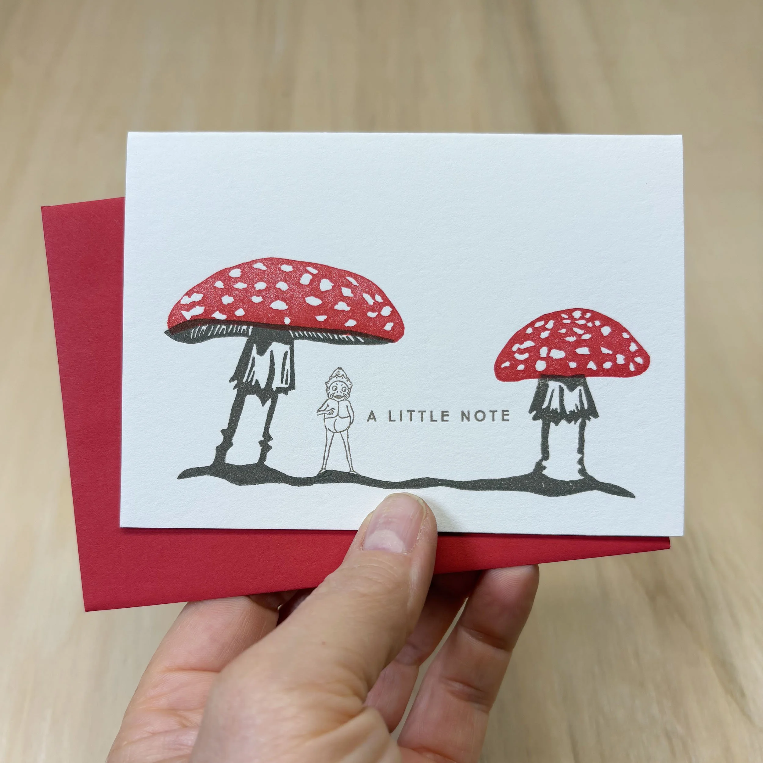 White notecard with illustration of two red capped mushrooms, a Palmer Cox Brownie, and the words A Little Note. Red Envelope.