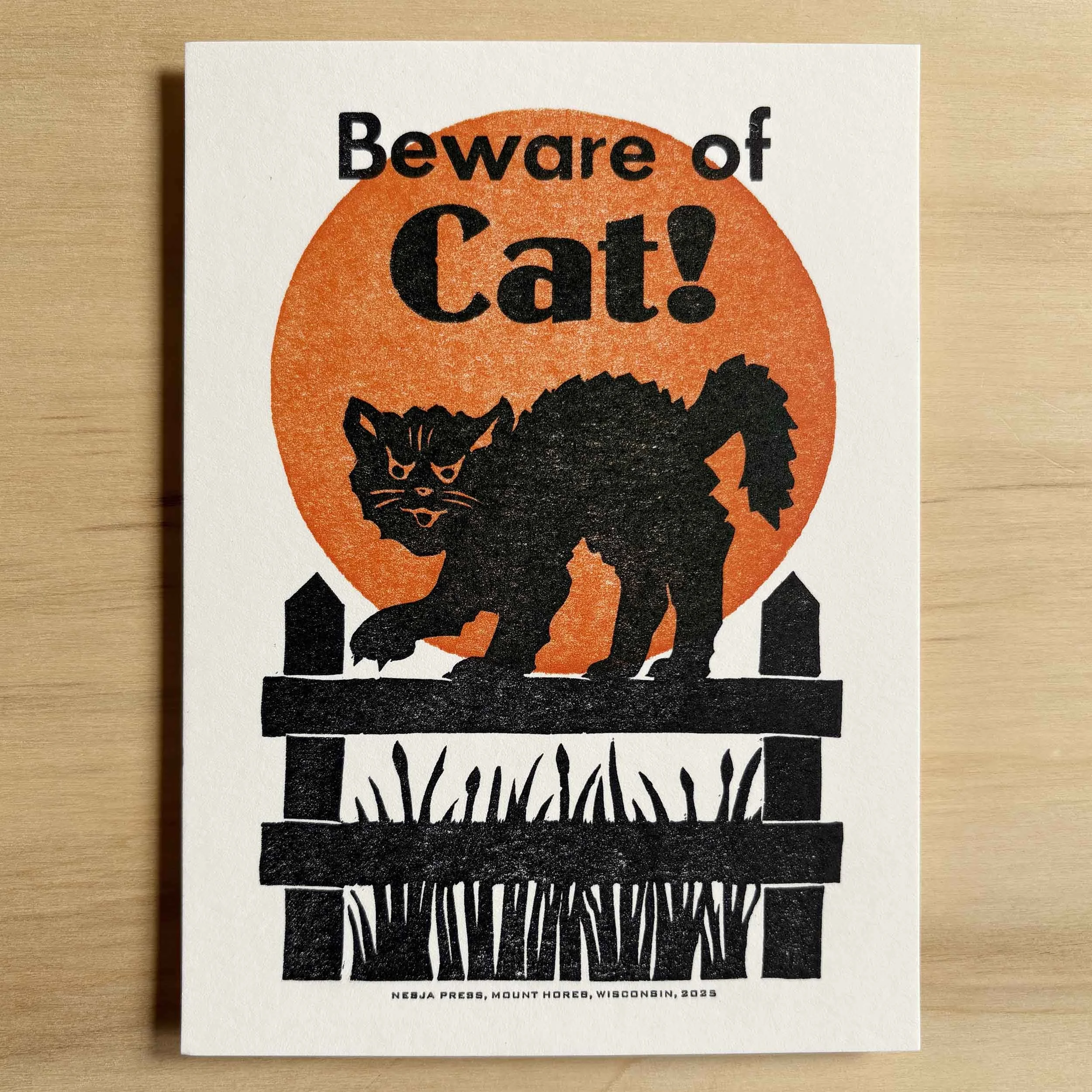 'Beware of Cat!' art print. Black text on white paper above a spooky black cat walking on a fence in front of an orange full moon.