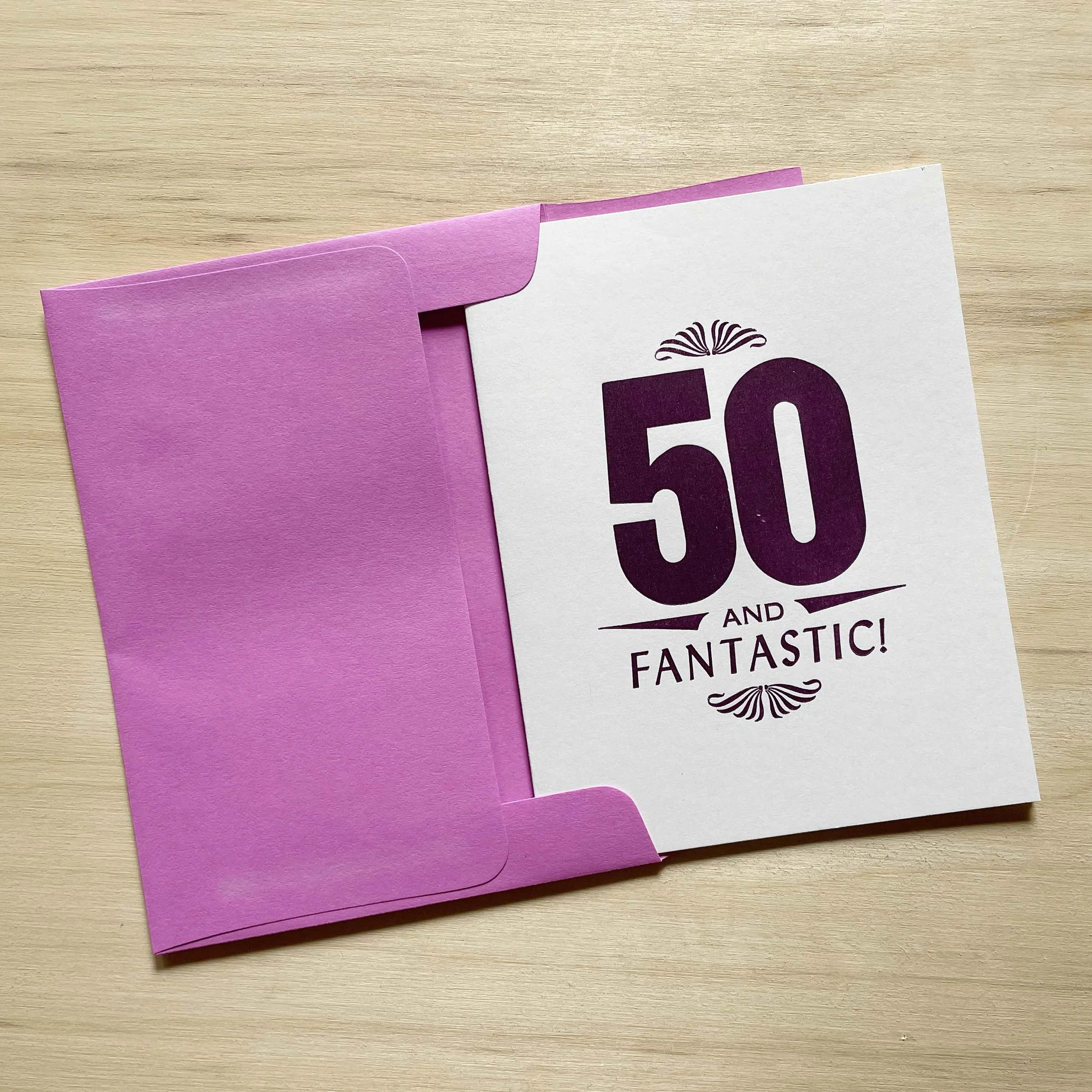 50 and Fantastic card features a bold 50 with smaller words AND FANTASTIC. Letterpress ornaments add decoration. Dark purple ink on white paper. Light purple envelope.
