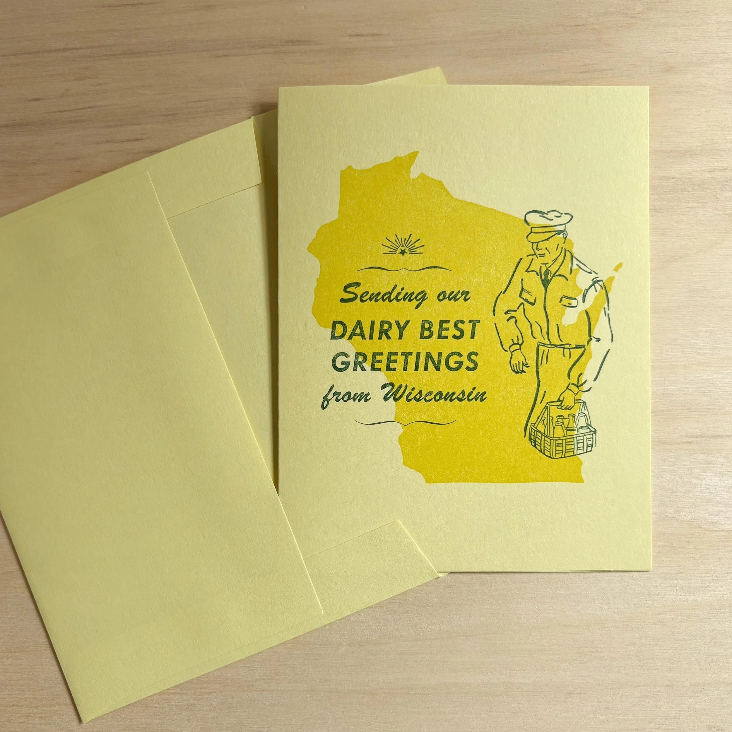 Handmade letterpress card with green type and a vintage milkman graphic printed over a solid yellow Wisconsin on light yellow paper.The words say 'Sending our dairy best greetings from Wisconsin.'