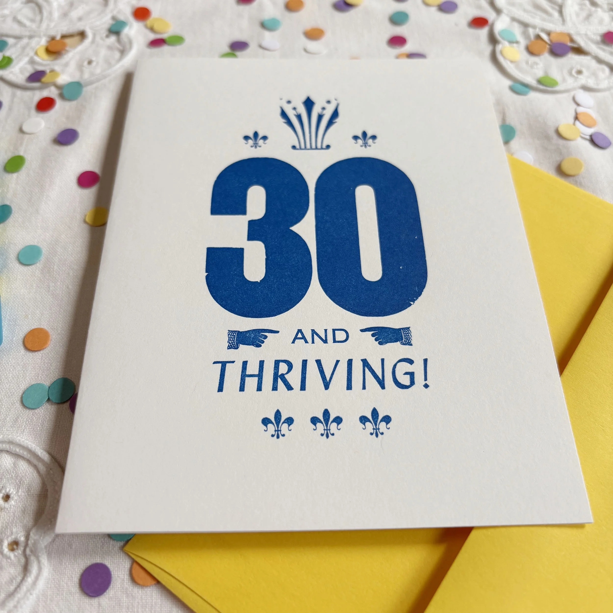 Thirty and Thriving card features a bold 30 with smaller words AND THRIVING. Letterpress ornaments add decoration and interest. Blue ink printed on crisp white paper. Bright yellow envelope.