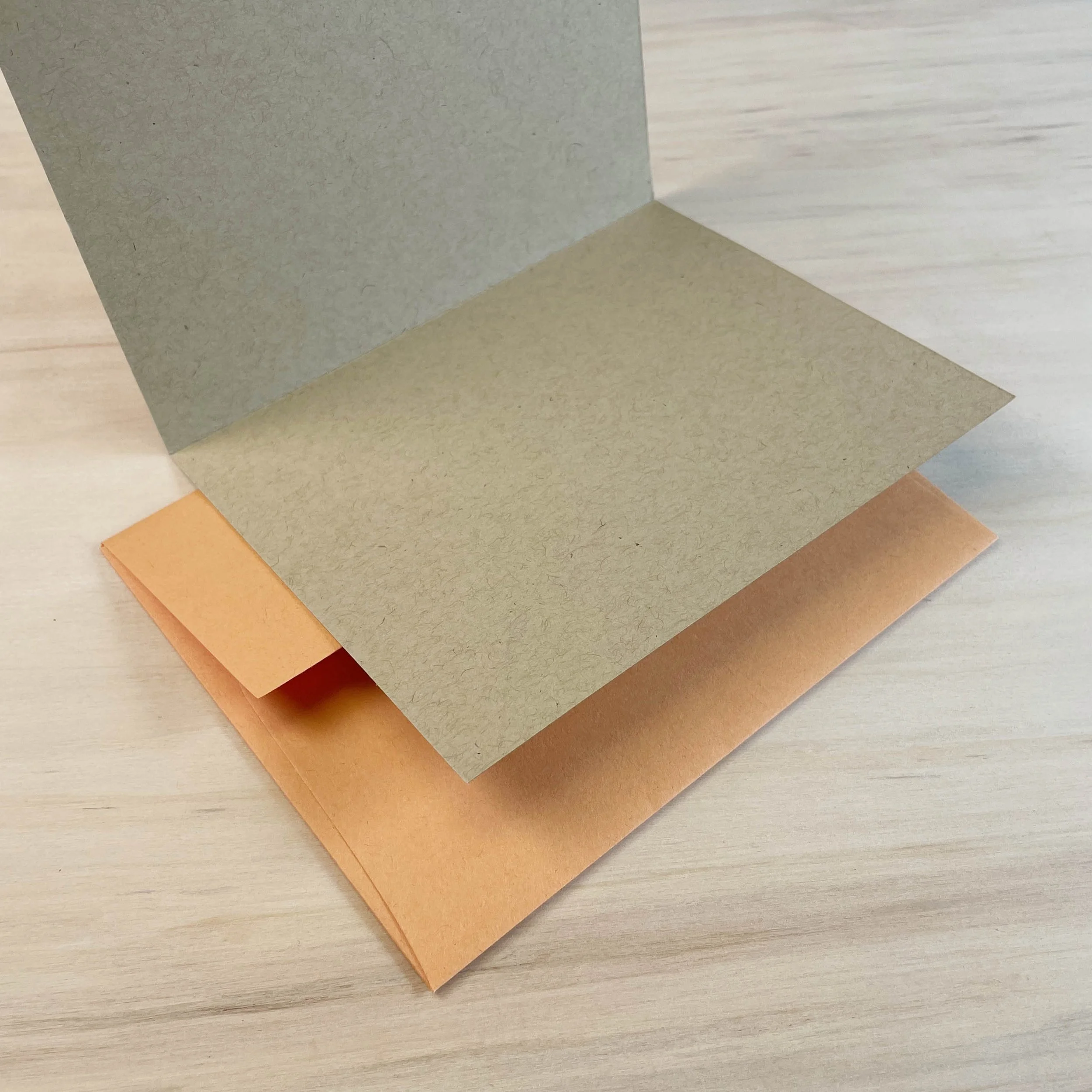 Kraft paper card opened to show blank interior, sitting on an orange envelope.