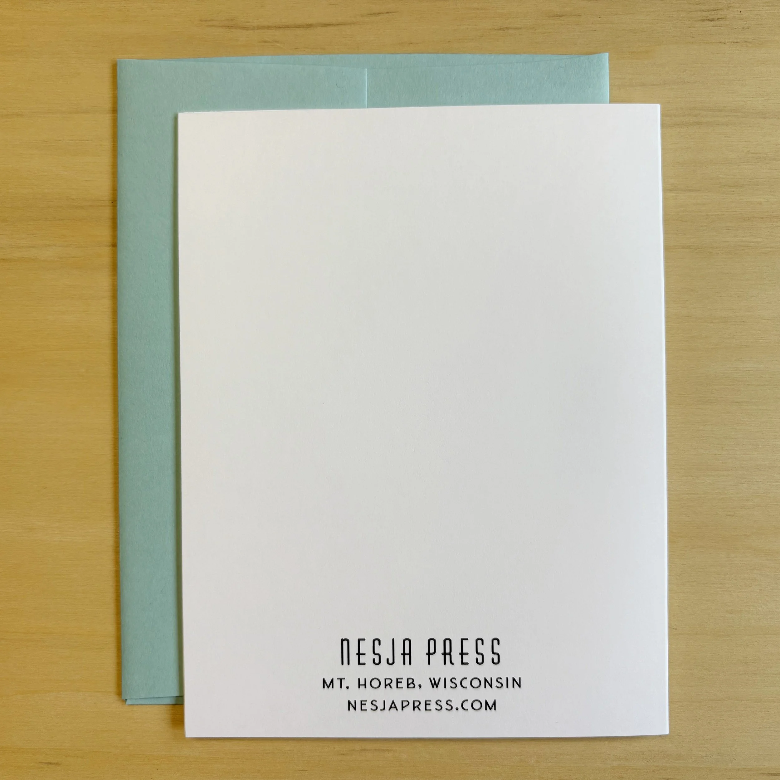Open closed showing back with Nesja Press logo and address.. Crisp white paper. Blue envelope.