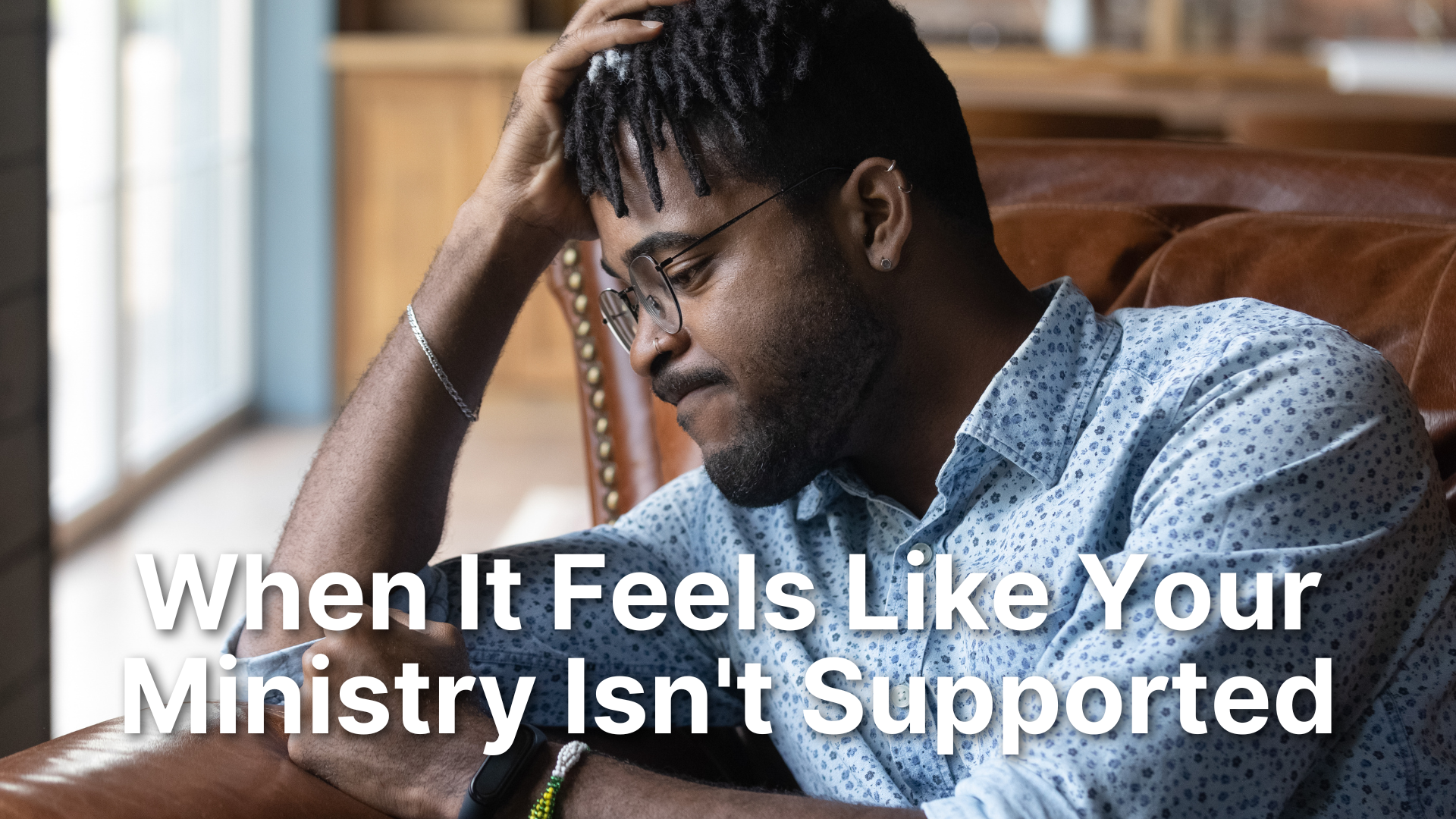 A discouraged-looking man in a blue patterned shirt and glasses sits on a leather sofa with his hand to his head, appearing stressed or deep in thought. Overlaid text reads: "When It Feels Like Your Ministry Isn't Supported".