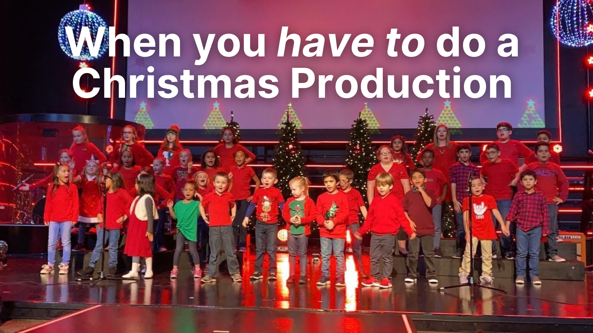 High-angle shot of a large group of smiling elementary school children performing a song on a brightly lit church stage decorated for Christmas. Large white text at the top reads, 'When you have to do a Christmas Production