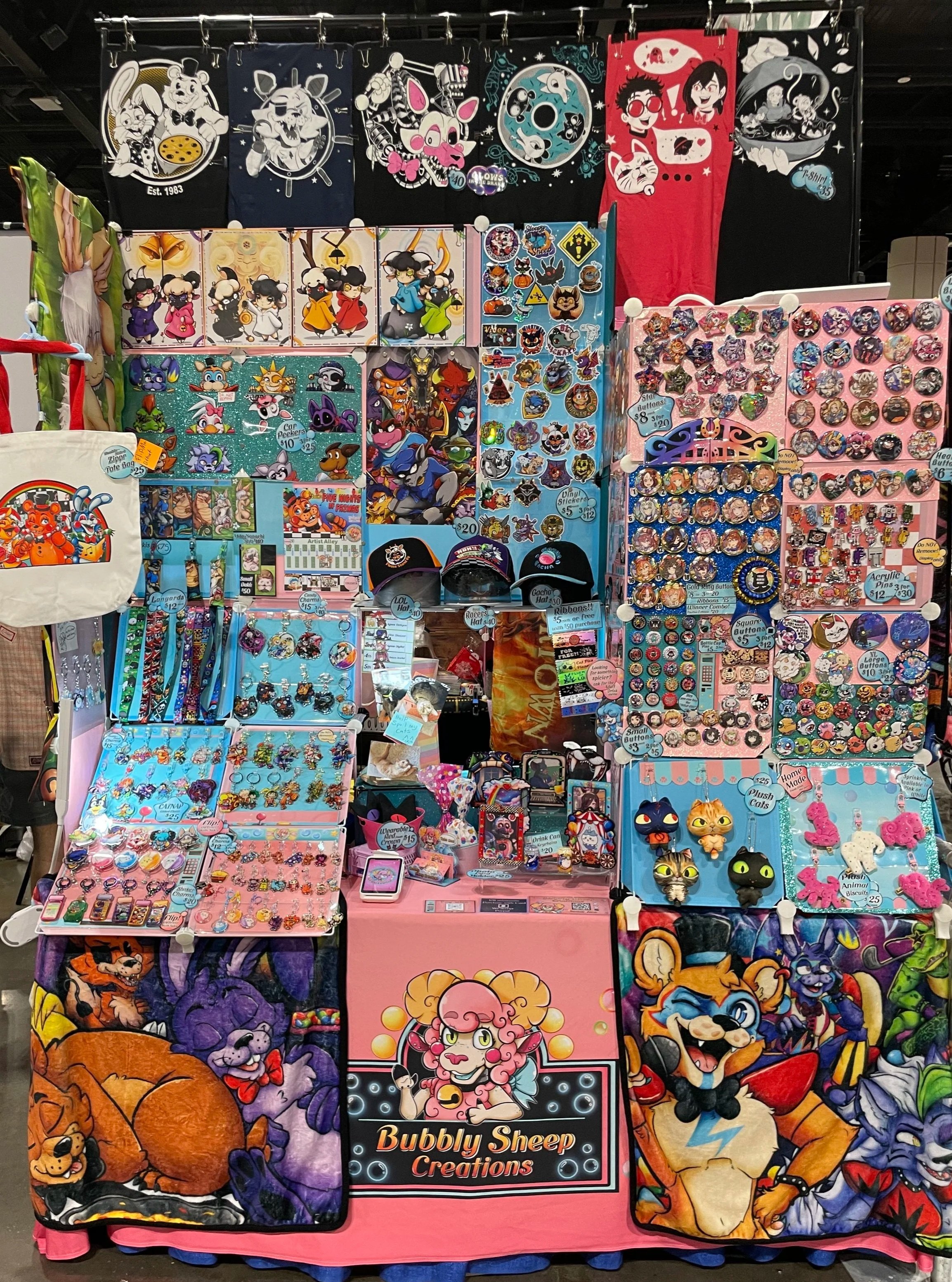 A colorful vendor booth displaying various cartoon-themed merchandise such as pins, keychains, plush toys, and hats featuring characters like cats, dogs, and other animated figures, with banners showcasing cartoon characters hanging above.