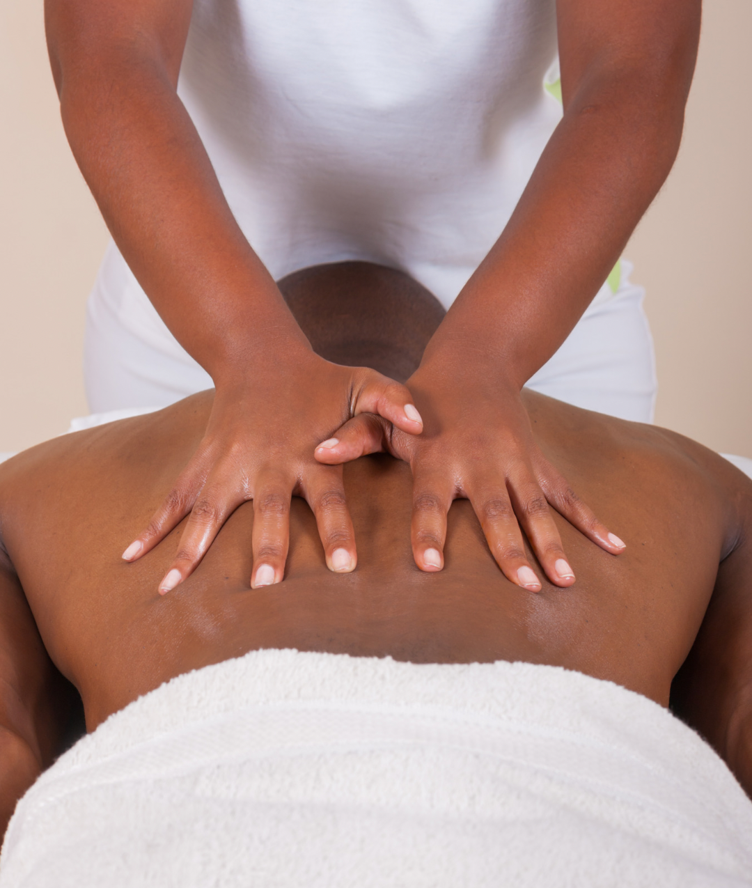 A person receiving a back massage with hands pressing on their back while lying face down on a towel.