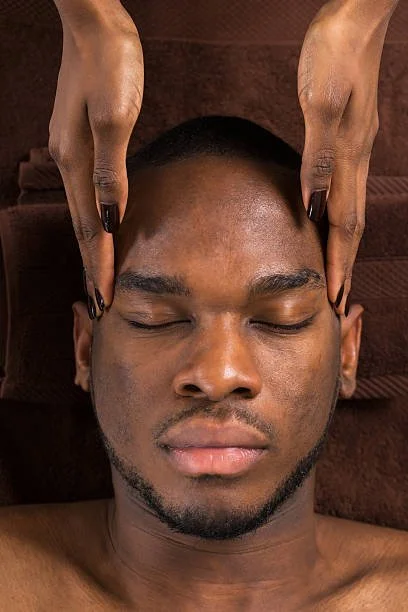 A man receiving a facial massage from a therapist with dark nail polish on their nails.