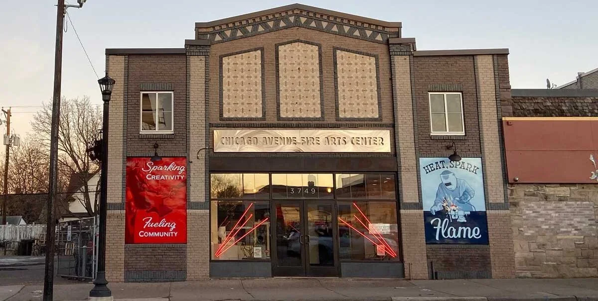 Exterior of the Chicago Avenue Fire Arts Center building, with three banners on either side of the entrance and neon lights in the windows.