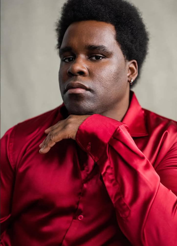 OJE BELO is an actor in the upcoming psychological thriller short film, THE LAST PERFORMANCE. This headshot features a smiling man with an afro hairstyle wearing a yellow shirt against a pink background.